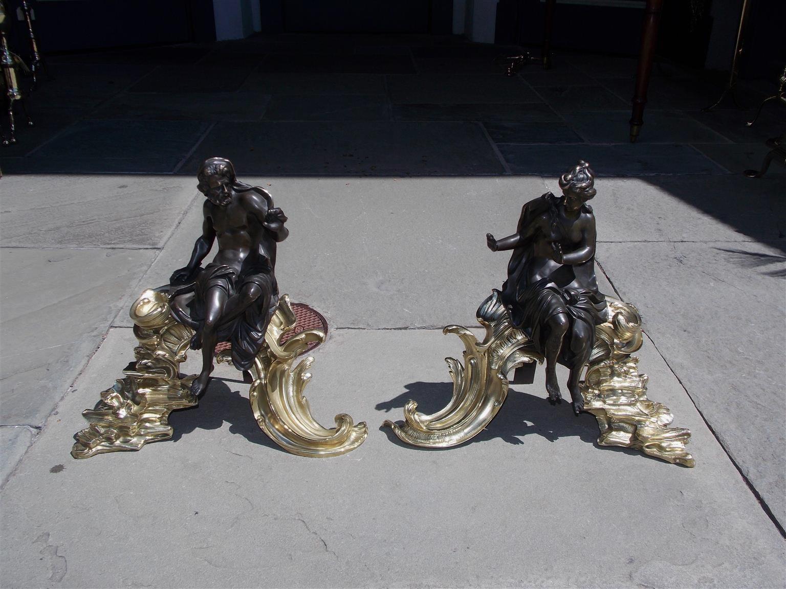 Pair of French bronze and brass mythological figural scrolled floral and step back rocky plinth chenets with supporting iron backs, Early 19th century.