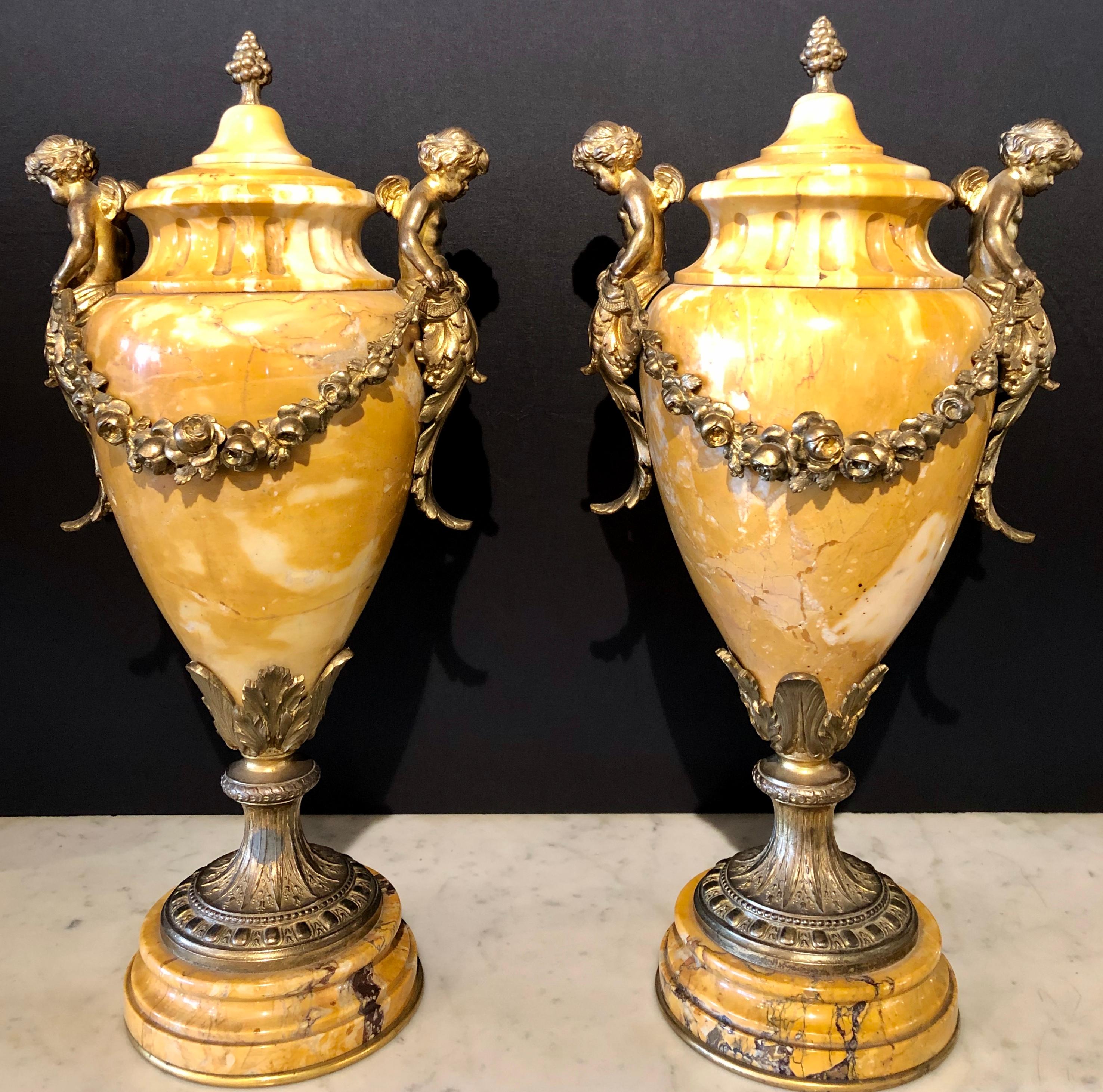 Pair of French bronze and marble Cassolettes each with cherubs having lids. These fine covered cassolettes with bronze putti mounted handles and valances, fluted top rim and tapered base to bronze and marble socle bases are certain to make a