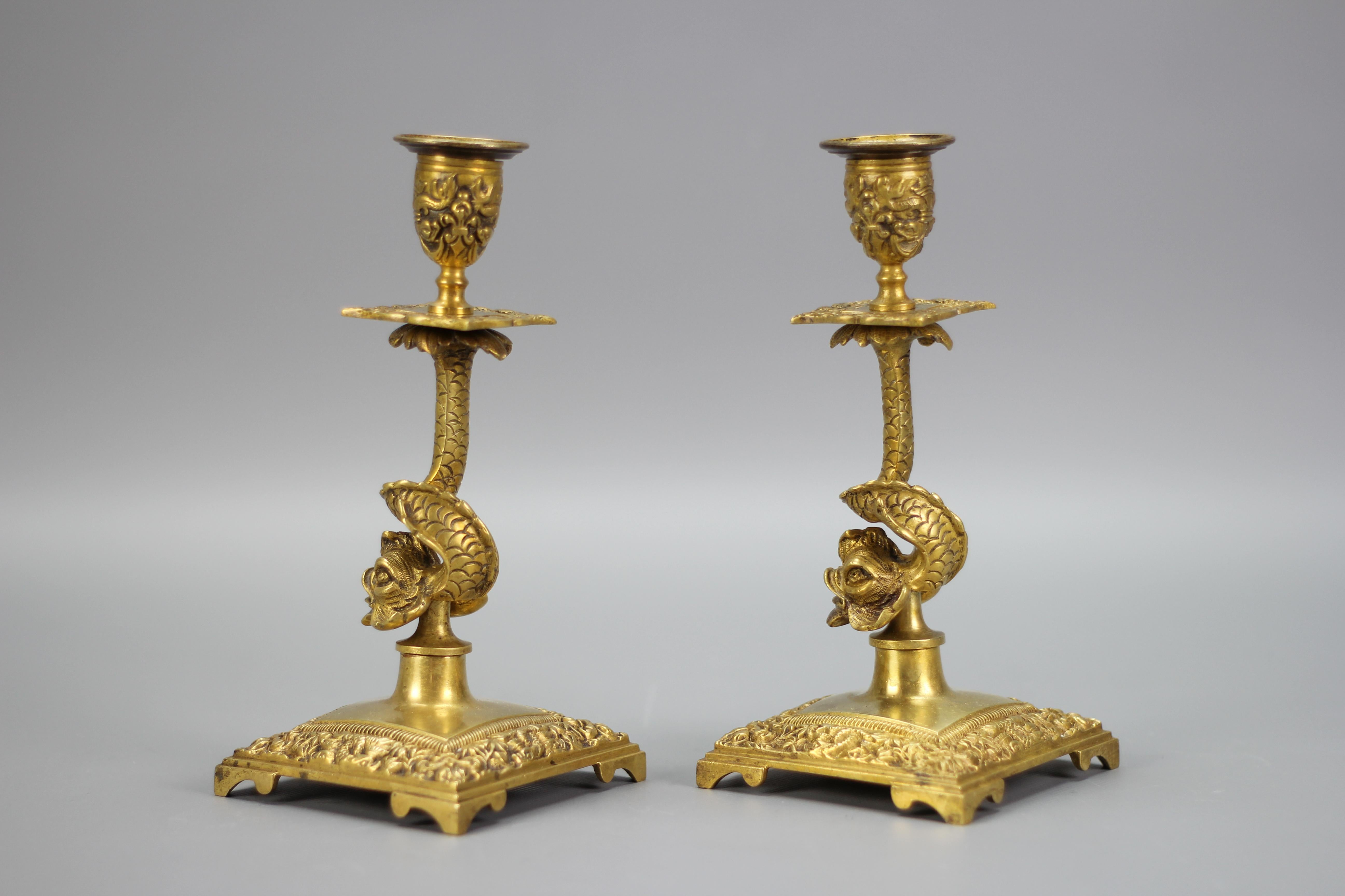 A pair of candle holders made of bronze, France, circa the 1930s.
These beautiful bronze candlesticks each feature column in the form of a dolphin. The square bases, wax pans, and sconces or capitals are richly ornate with foliate and dolphin