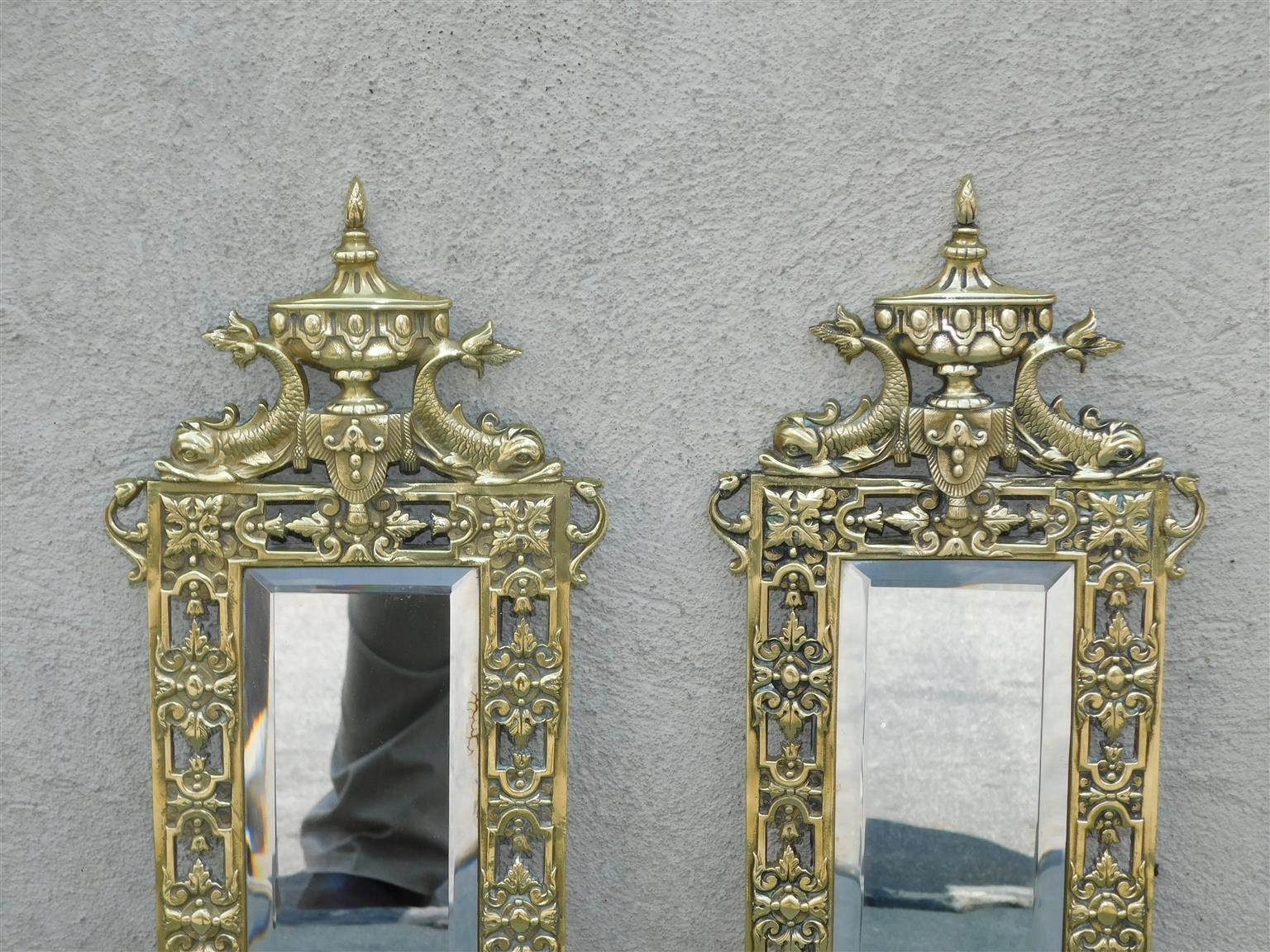 Coppia di appliques a specchio con urne centrali e delfini affiancati, in bronzo, con bordi a medaglione con fogliame, nappe decorative, due bracci a voluta con fogliame e conservano gli specchi originali smussati, inizio XIX secolo

Attualmente le