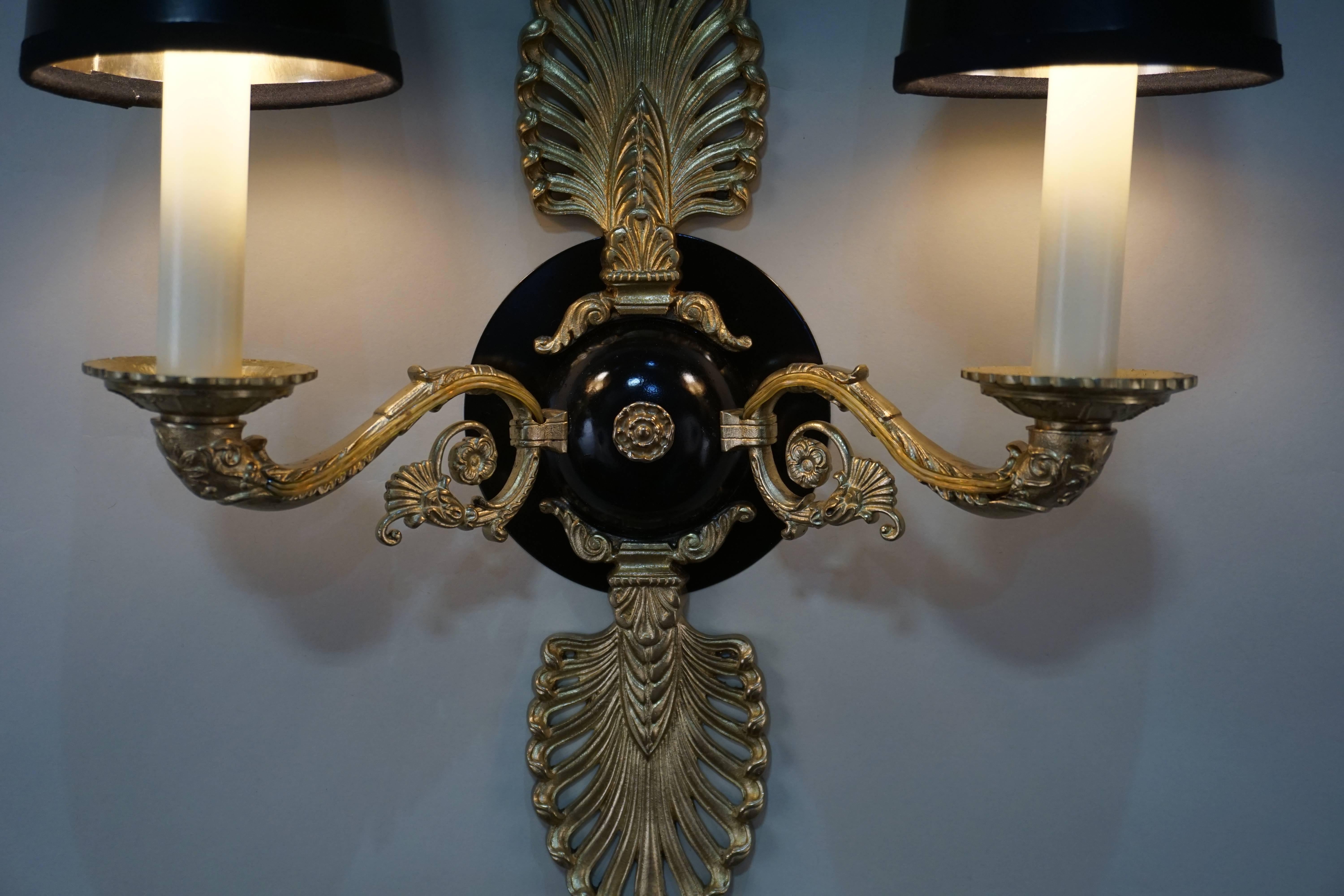 A wonderful pair of double arm wall sconces. Made in France during the early 30th century, the sconces feature a Classic Empire style design. The beautiful bronze work is filled with intricate detail and craftsmanship. The black lacquer centre gives