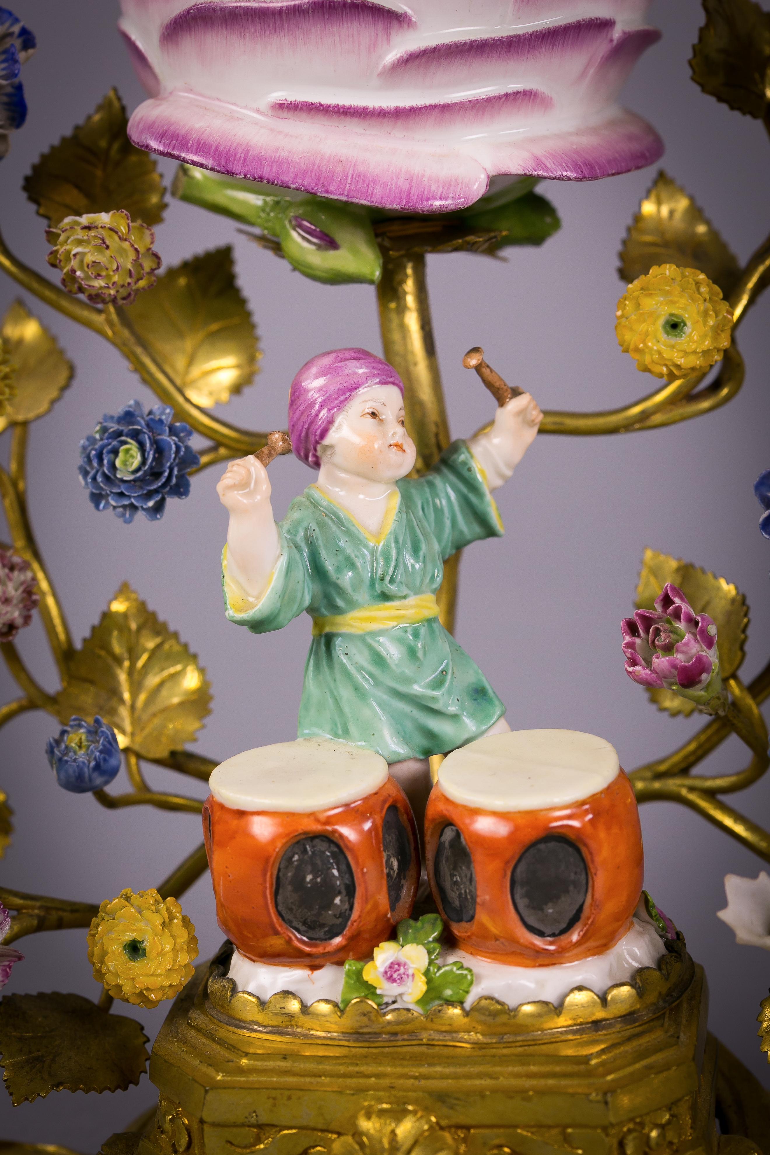 Each with a figure of a turbanned boy playing drums with porcelain flowers and a cabbage flower with a removable lid.