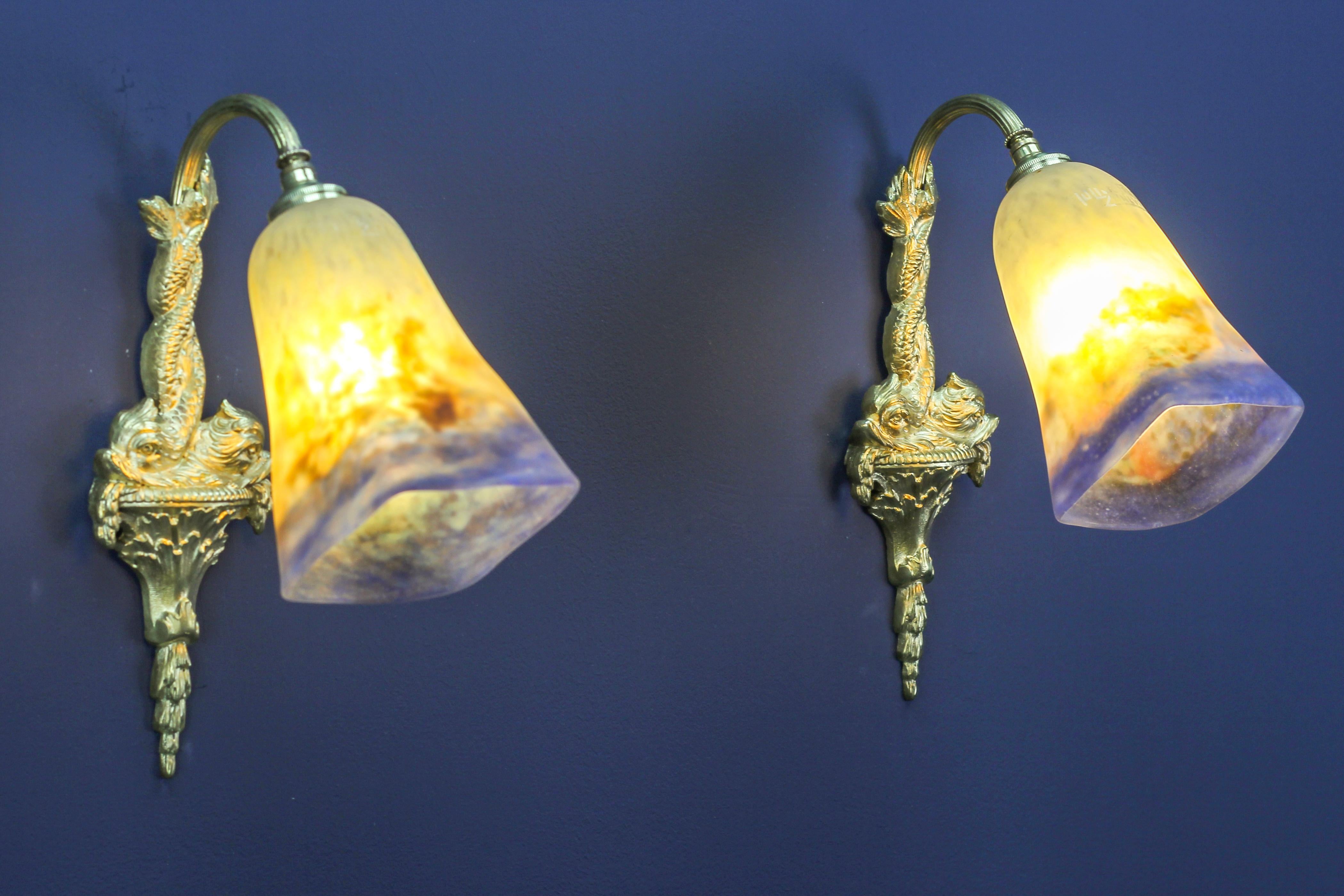 Pair of French bronze sconces with dolphins and Muller Fres Luneville glass.
A beautiful pair of bronze sconces each with motifs of two dolphins and “Pâte de Verre” glass lampshades in white, blue, orange, and olive green tones, each signed Muller