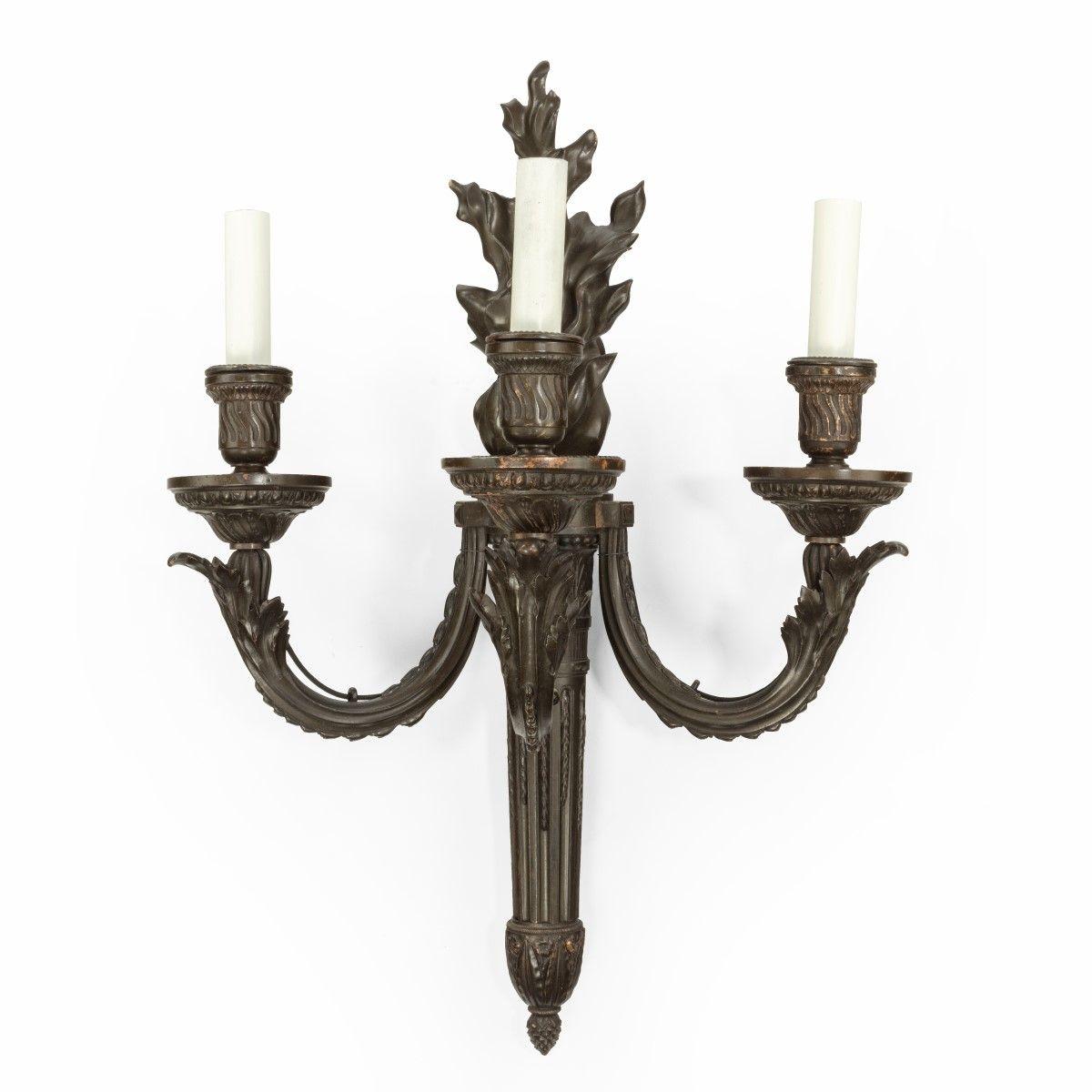 A pair of French bronze wall-lights, each in the form of classical torch with a flambé top supporting three arms, decorated with stop-fluting and classical motifs, now fitted for electricity. Circa 1880.