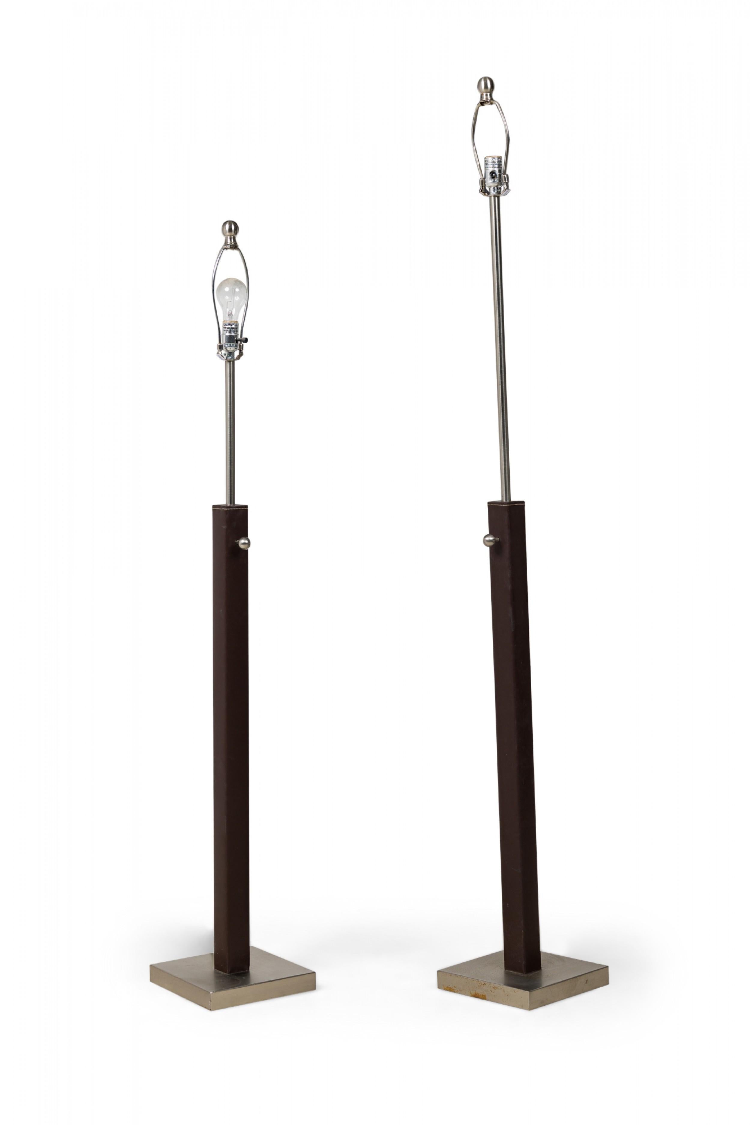 PAIR of French midcentury-style matched floor lamps in staggered heights, with brown stitched leather and brushed silver metal posts, resting on square brushed metal bases. (manner of Jacques Adnet)(PRICED AS PAIR).