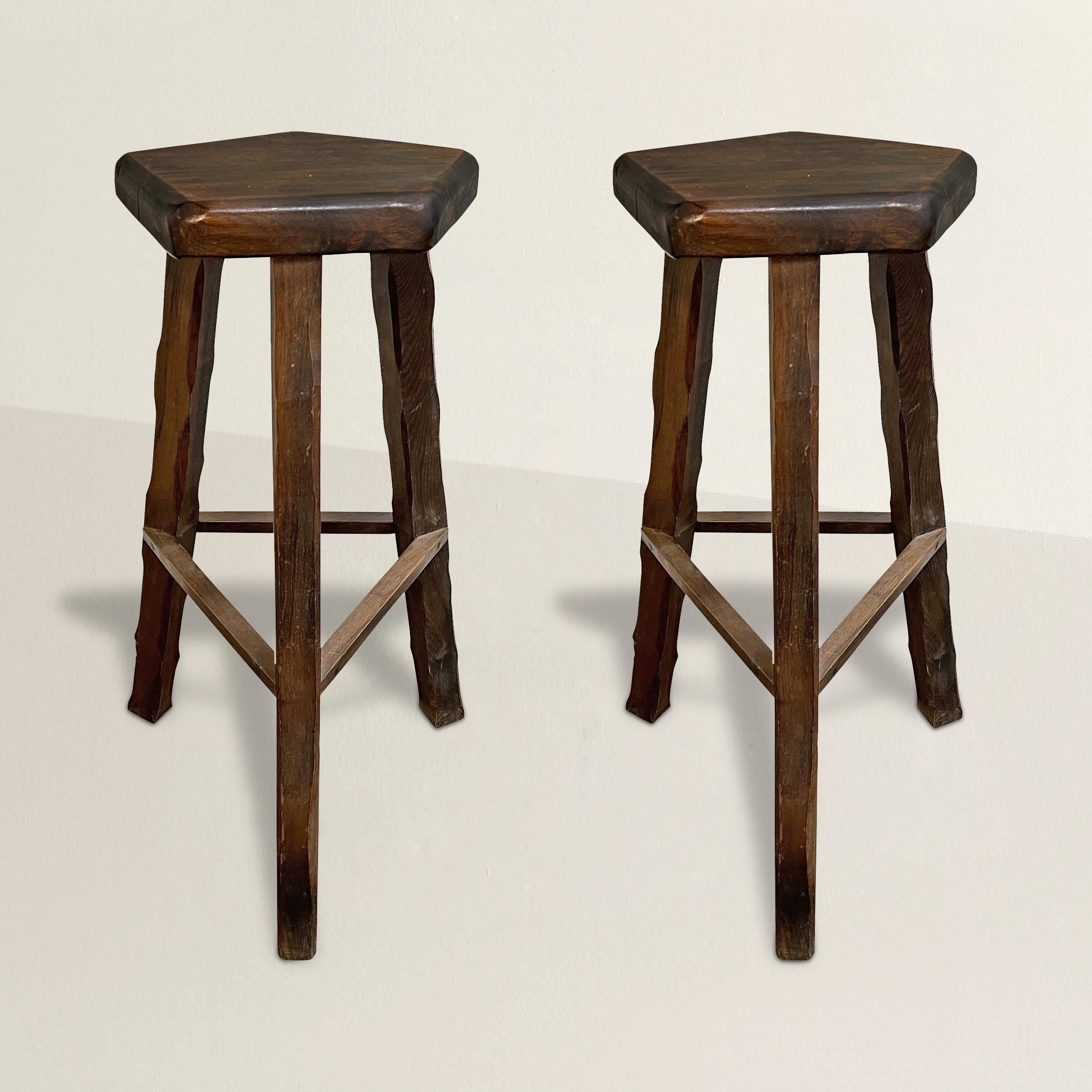 Embrace the raw and captivating allure of French Brutalist design with this extraordinary pair of oak bar stools. These stools embody the essence of the movement with their chunky pentagonal seats, and played chamfered legs, which exude a sense of