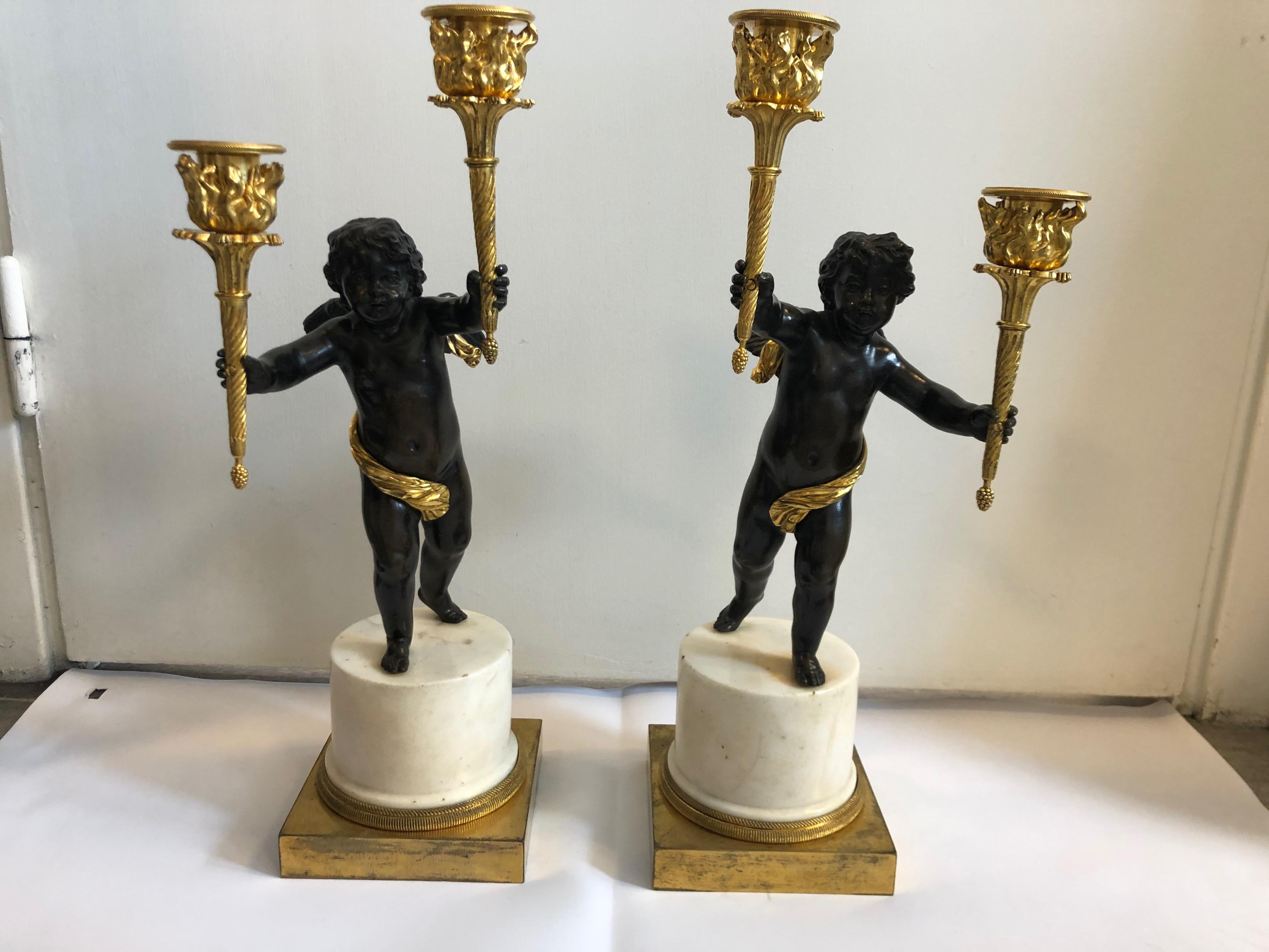A pair of French candelabra, gilt and black patinated bronze together with white marble. Puttis standing on columns holding torches in both hands.