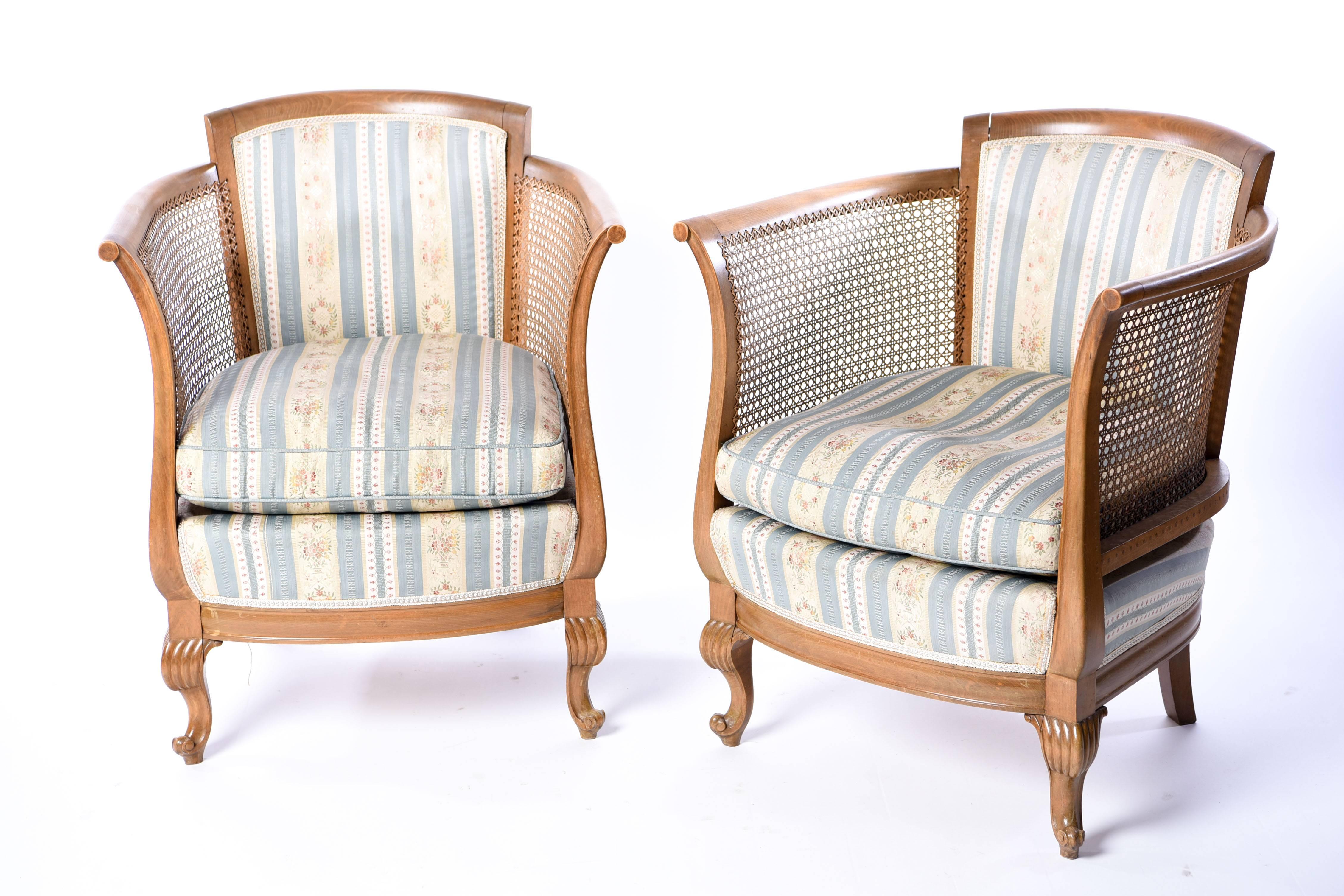 This pair of French bergere armchairs features upholstered seats and backs with curved caned sides. Beautiful ribbed design on the Rococo style legs.