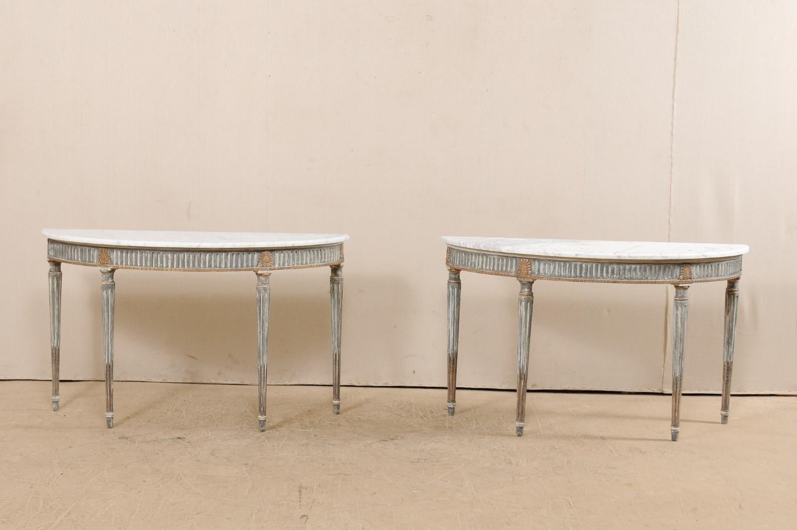 A pair of French carved and painted wood demilune tables with marble tops from the mid-20th century. These beautiful pair of antique half-moon console tables from France are adorn with interpretive neoclassical carved elements, with a decoratively