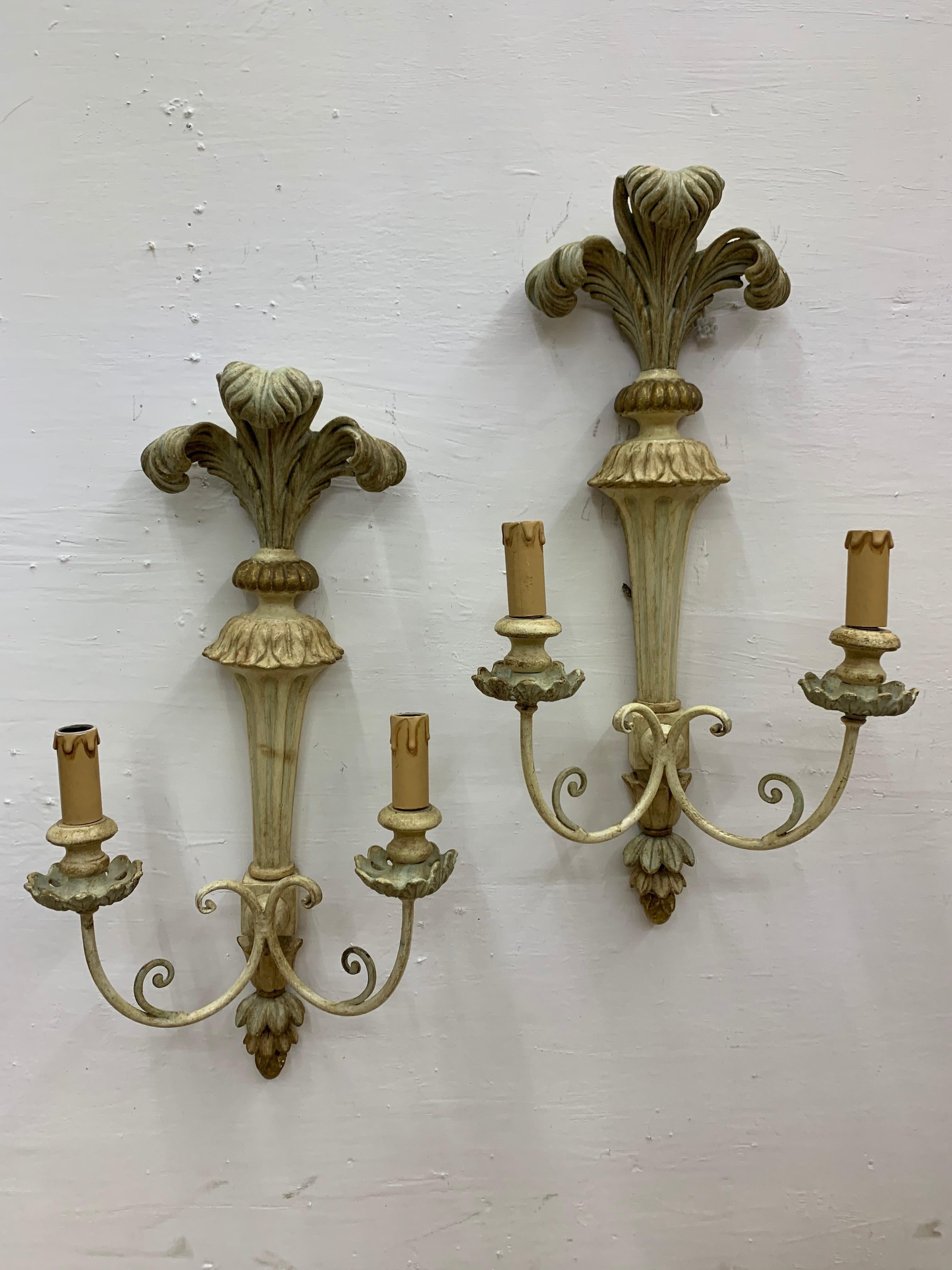 Beautiful pair of large two light sconces in iron and wood carved with classical motifs such as the ostrich plume finial, gilded and painted in pastel tones. 
Made in France, circa 1950.