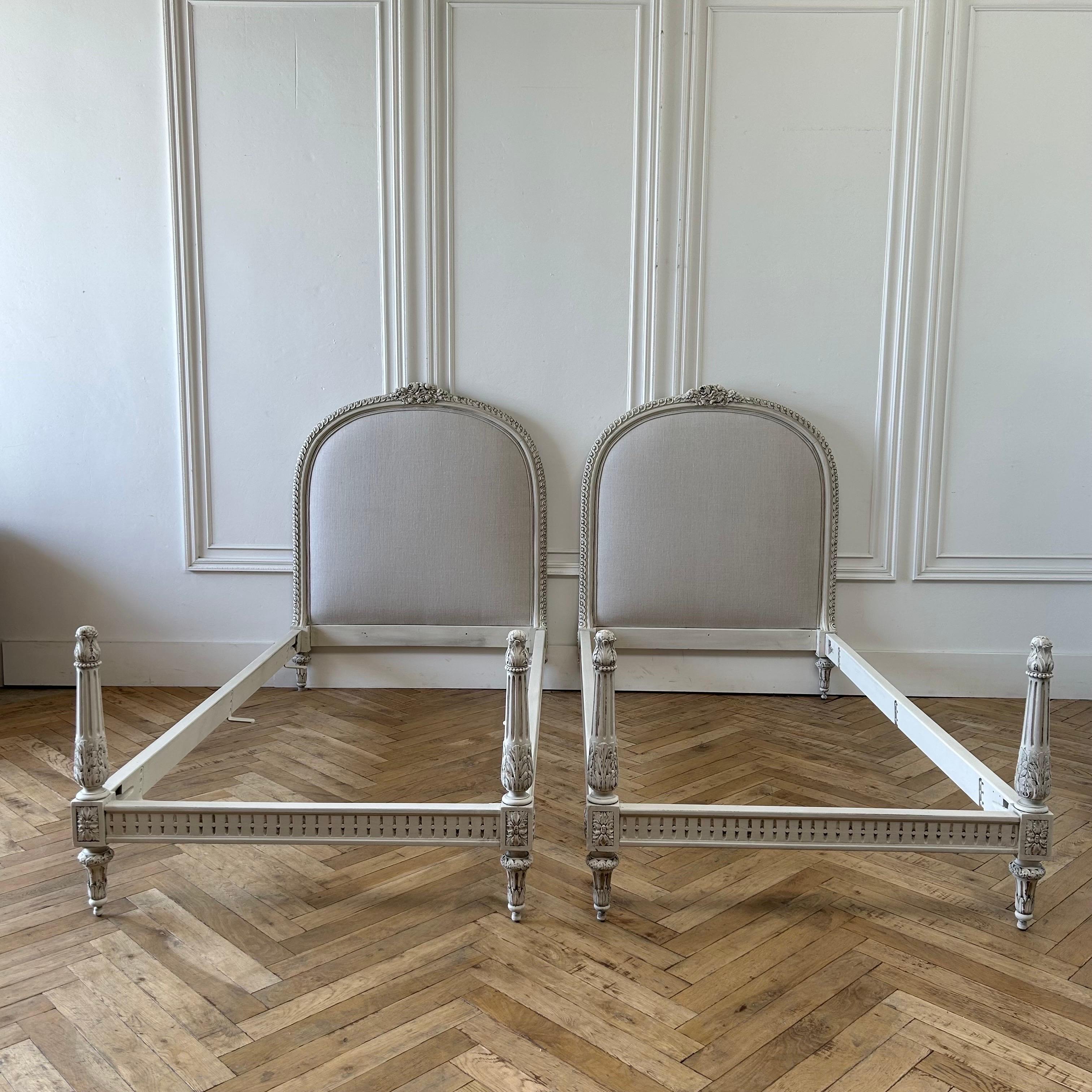 Beautiful French twin beds painted in an antique white, with distressed finish, and antique glazed patina.
We upholstered them in a natural oatmeal Libeco Belgian linen.
Original wood rails and slats. Very solid and sturdy when assembled.

Pair twin