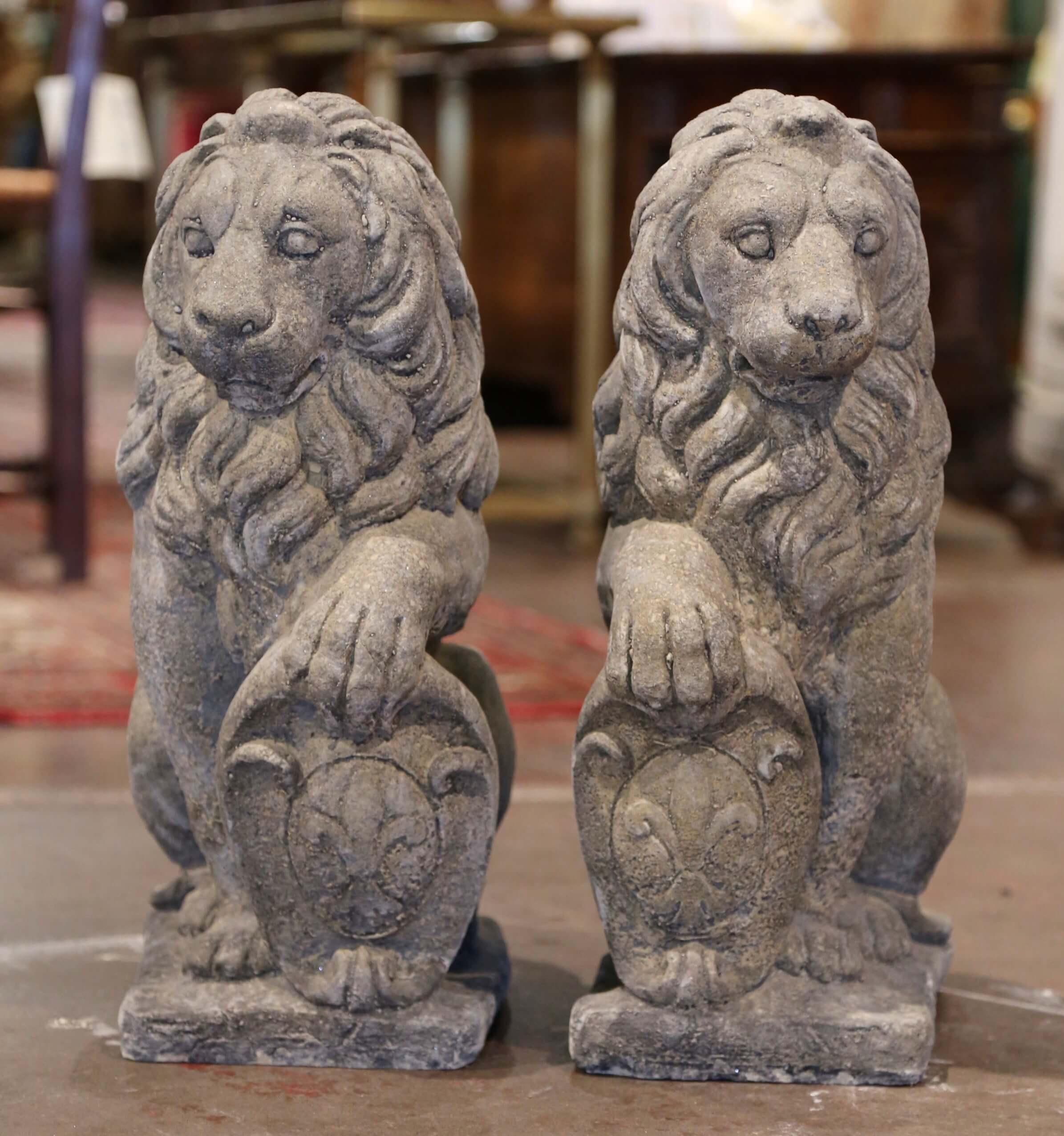 Carved of stone in France circa 2000 and set on a rectangular integral base, the vintage feline statues are seated on their back legs while holding a Fleur-de-Lys shield with one paw. The Westcott felines have wonderful expression with long hair and