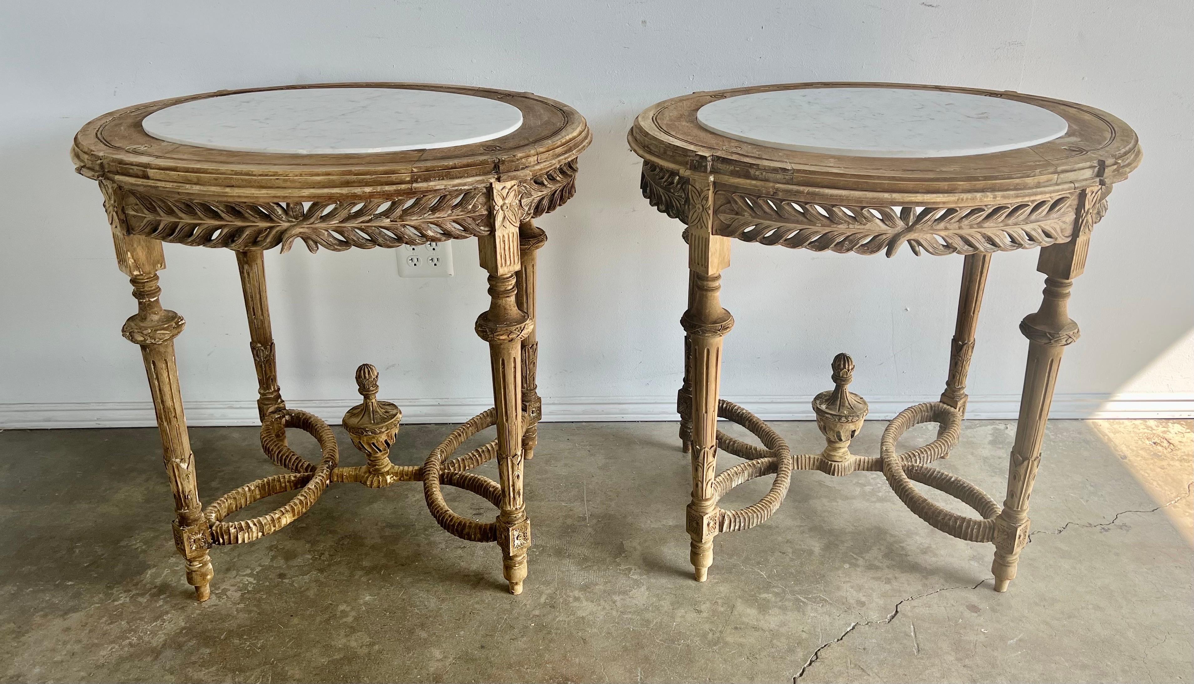 Pair of early 20th century bleached wood oval shaped French Provincial style tables with inset white marble tops. The tables stand on four straight legs with a unique braided rope stretcher that has a carved wood urn in the center. They have white