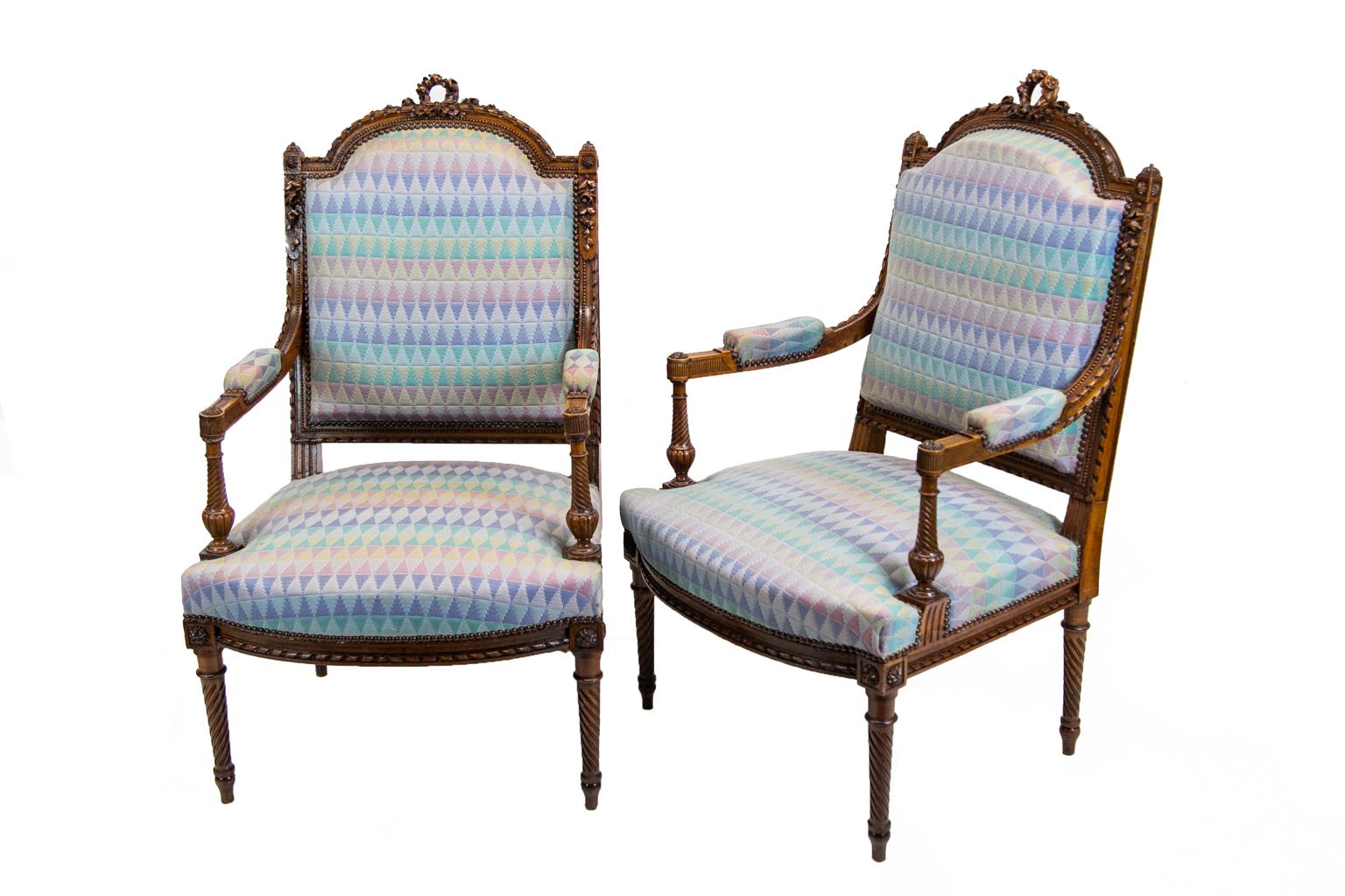 Pair of French carved walnut bergère armchairs have upholstery framed with brass stud work all around. The arms are carved with beadwork, a spiral ribbon, and leaf and flower designs carved in high relief. They also have carved ribbing and a carved