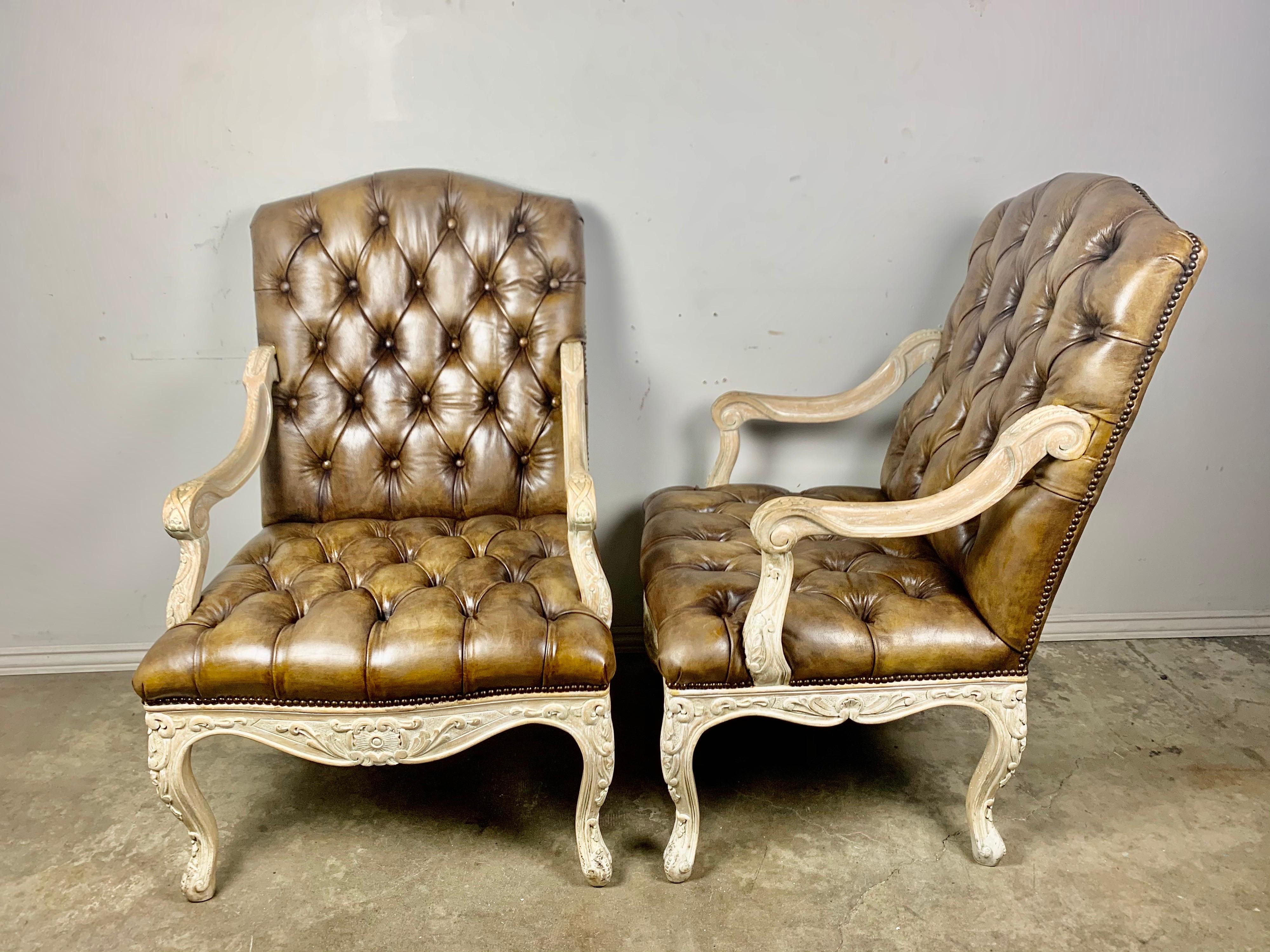 Pair of 1940s French carved wood armchairs that are upholstered in tobacco colored leather and finished with antique brass colored nailhead trim detail.