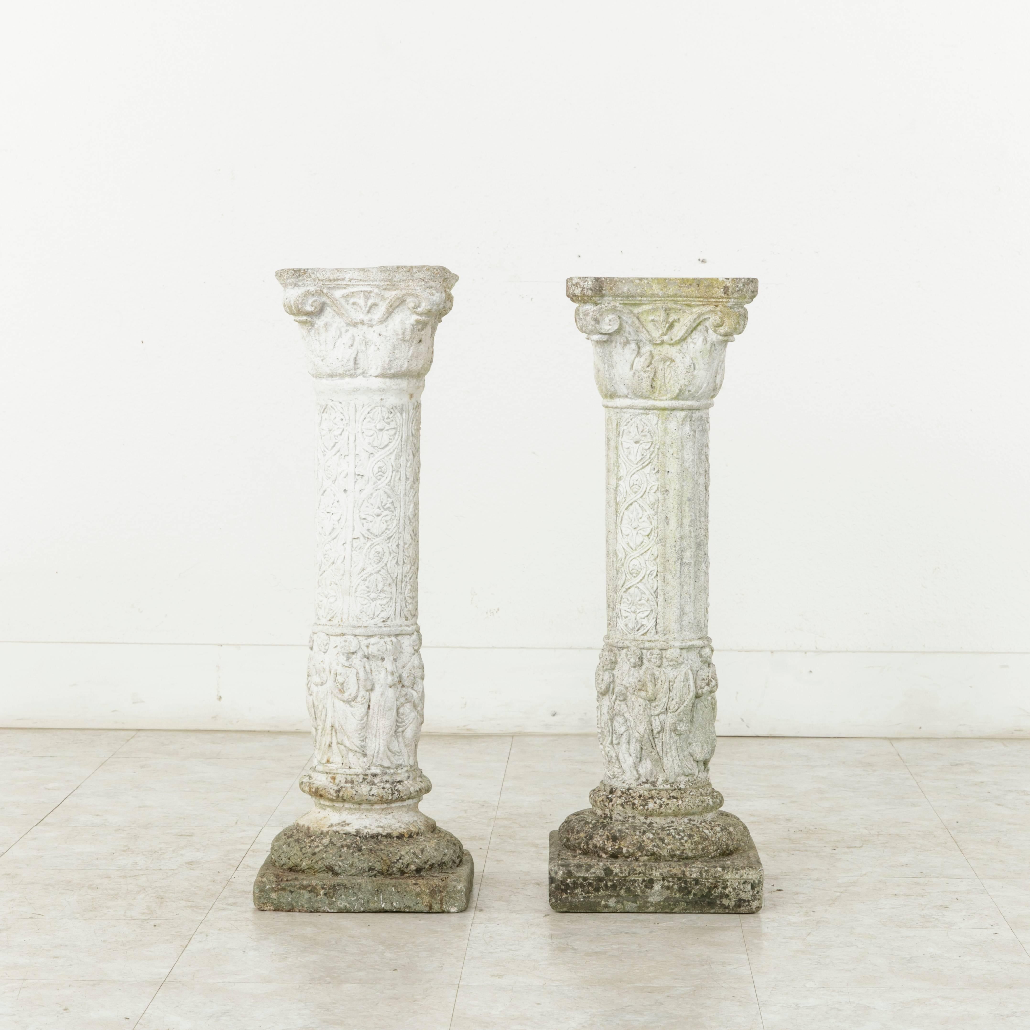 This pair of cast stone columns or pillars from the mid-20th century originally graced the gardens of a manor house in Normandy, France. Motifs of classical figures surround the base of the columns with interlaced rosettes above. A false pair, one