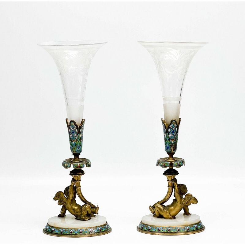 Pair of French Champleve enamel bronze putti engraved glass trumpet form vases.

Pair of French Champleve enamel gilt bronze putti mounted engraved glass trumpet form vases, late 19th century. Clear glass vases with etched floral and garland