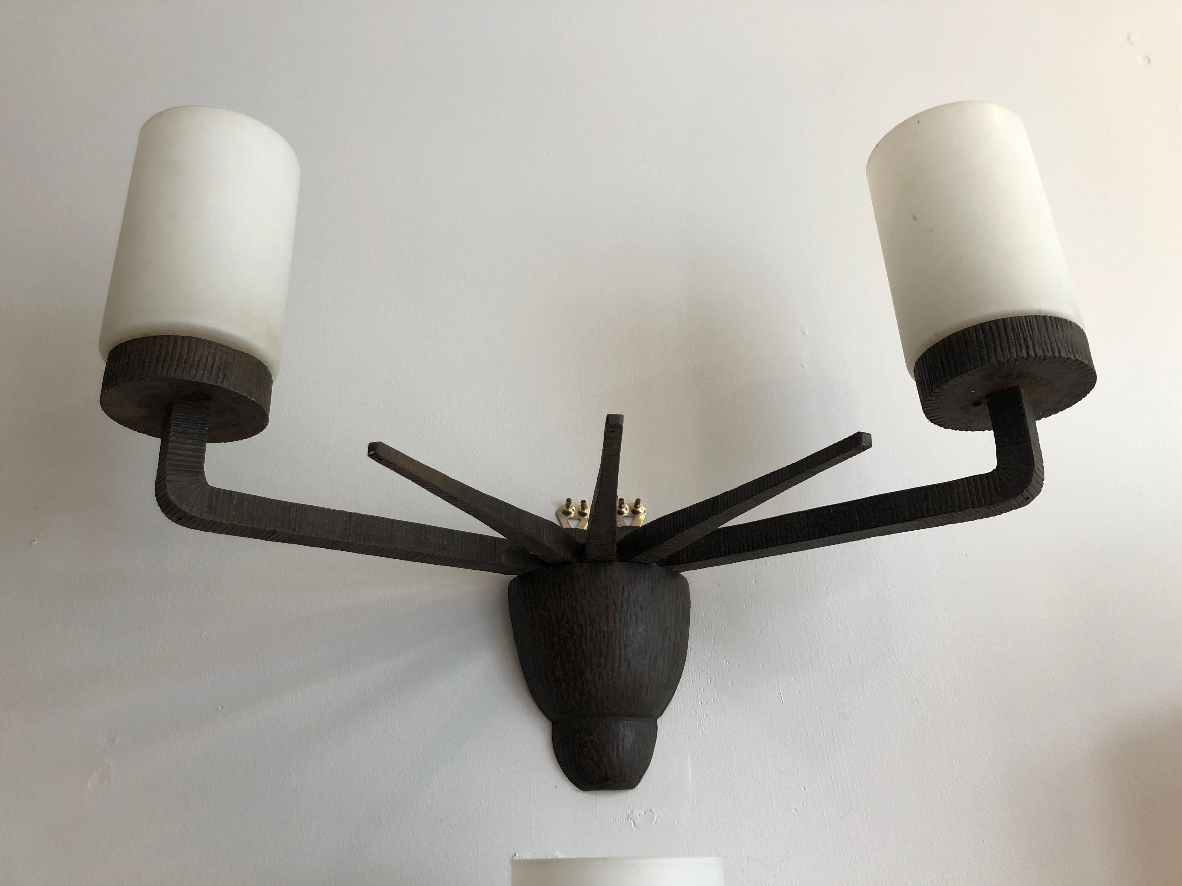 Art Deco modernist Gothic design recalls the Statue of Liberty, with its spiked crown and raised torches. Hand-worked wrought iron two-arm sconces, with original patina and milk glass shades. Unsigned, but high quality craftsmanship.