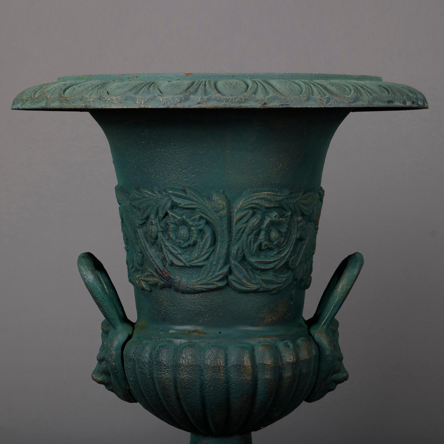 A pair of well cast French Classical garden planters feature iron construction in pedestal urn form having double handles, melon bowl bases and bands of high relief foliate decoration, painted green, seated on flared plinths having reserves with