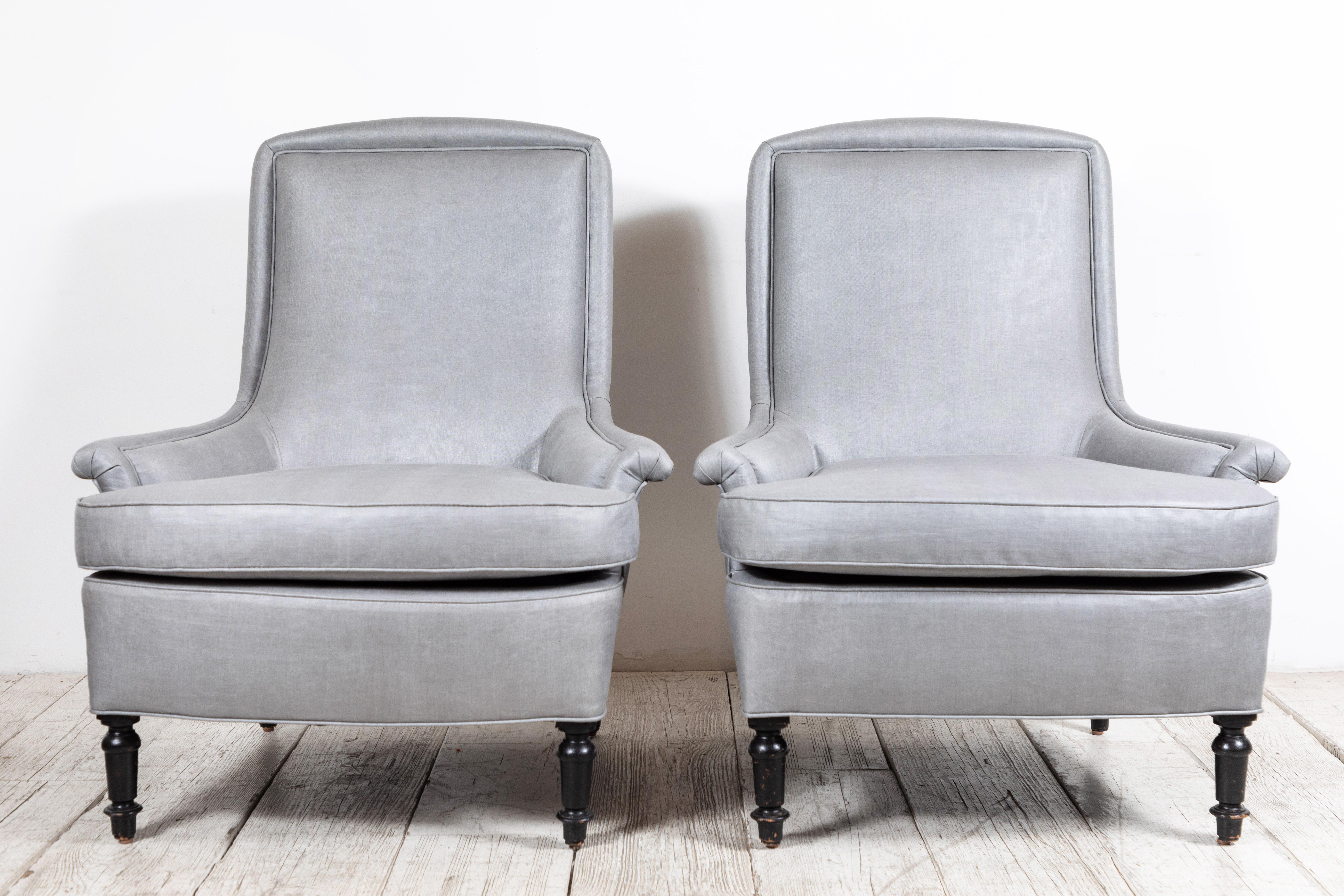 Pair of French club chairs with beautiful scrolled arms and unique piping details. Newly upholstered in grey beetled linen by Howe of London. Original turned black painted legs.