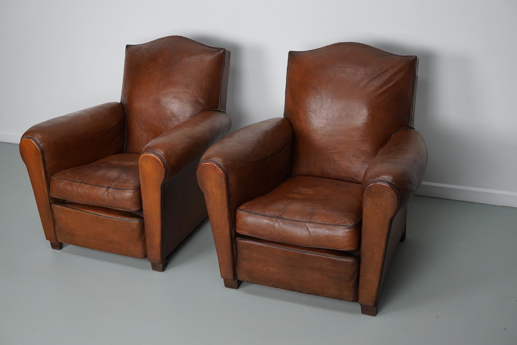 These club chairs were designed and produced in France during the 1940s. The chairs are made from cognac leather held together with metal pins and mounted on wooden legs.