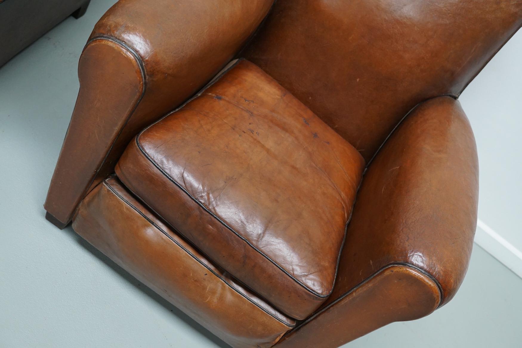 These club chairs were designed and produced in France during the 1940s. The chairs are made from cognac leather held together with metal pins and mounted on wooden legs. The springs and straps have been replaced by special foam and new straps so