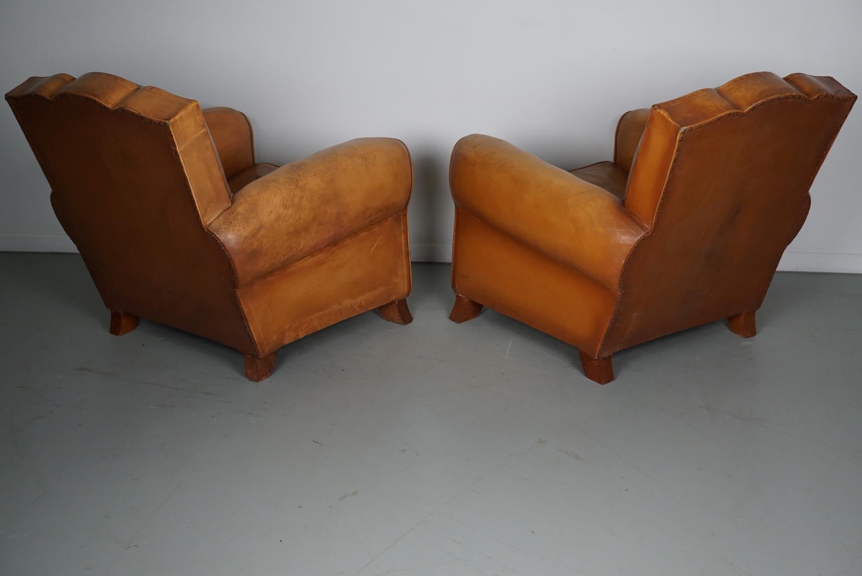 These club chairs were designed and produced in France during the 1950s. The chairs are made from cognac leather held together with metal pins and mounted on wooden legs.