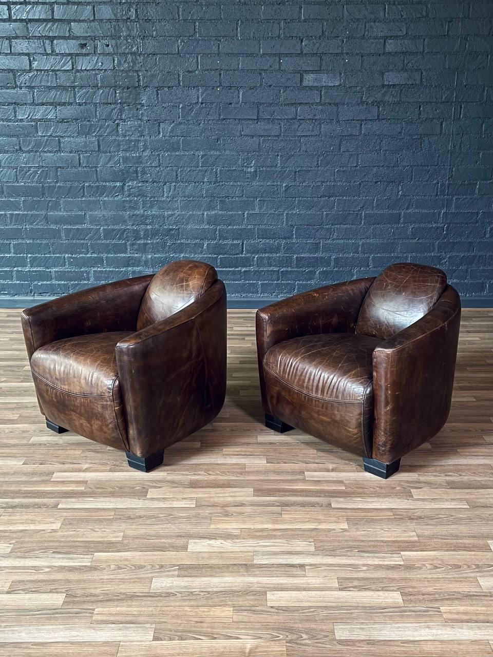 Condition: Original Condition 
Materials: Leather, Ebonized Wood Feet

This pair of French Contemporary Art Deco style leather club chairs combines timeless elegance with modern comfort. Upholstered in rich, well-patinated leather, they feature a