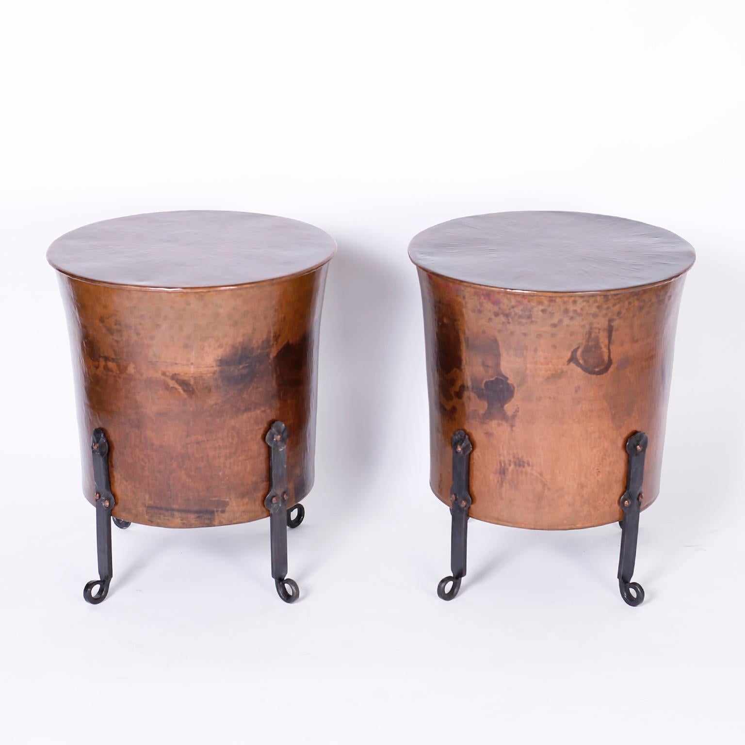 Antique pair of copper and iron stands with hand hammered copper tapered drums having acquired a lofty patina and riveted to four hand hammered graceful iron legs.