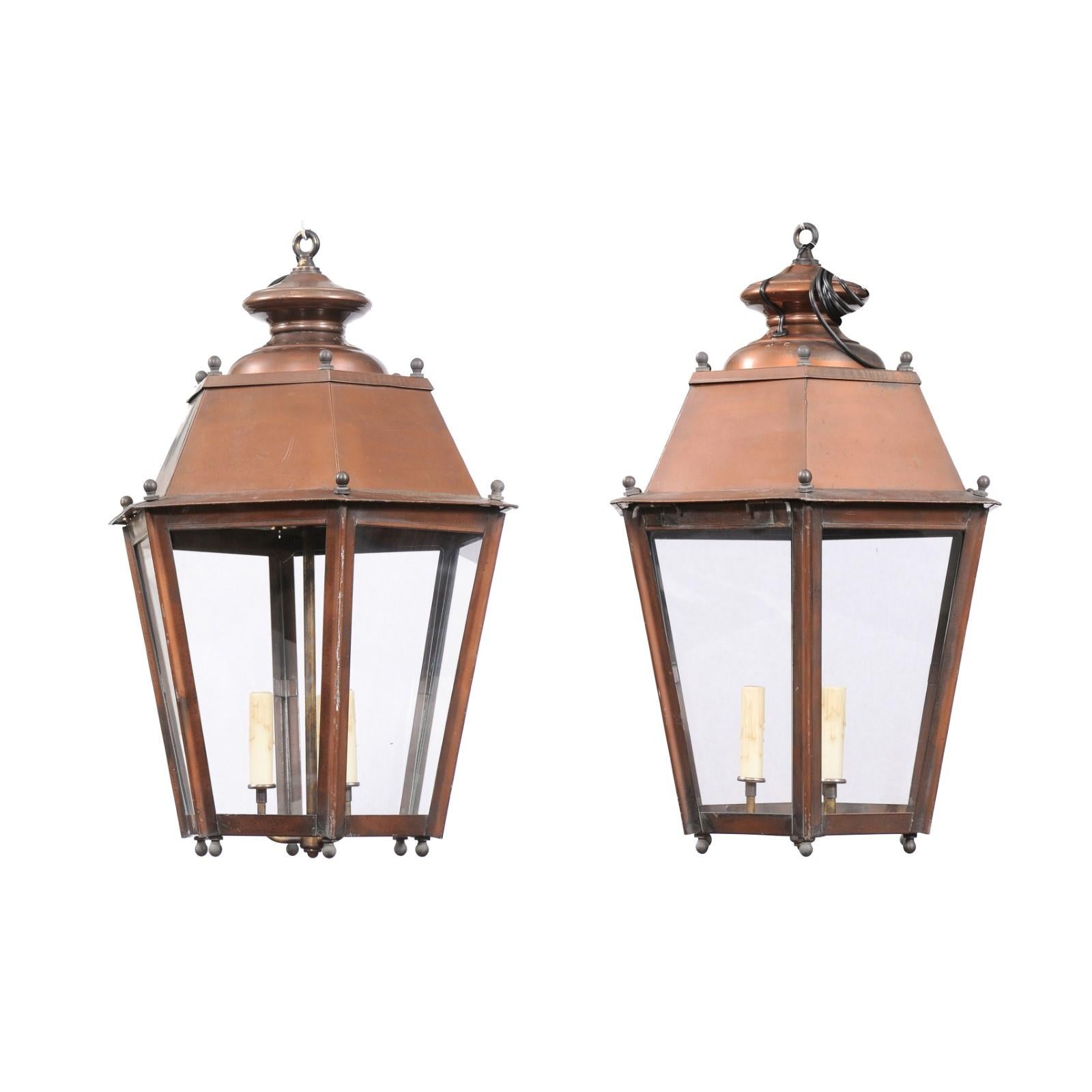 A pair of French hexagonal three-light copper lanterns from the 20th century with tapered lines, glass panels and petite spheres. Introducing a captivating pair of French hexagonal copper lanterns from the 20th century, a testament to timeless