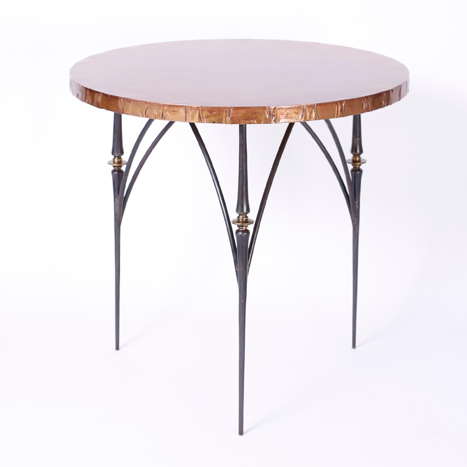 Pair of midcentury tables with hand hammered copper round tops having acquired a time worn patina over three elegant legs featuring turned brass ornaments and architecturally interesting arched supports.