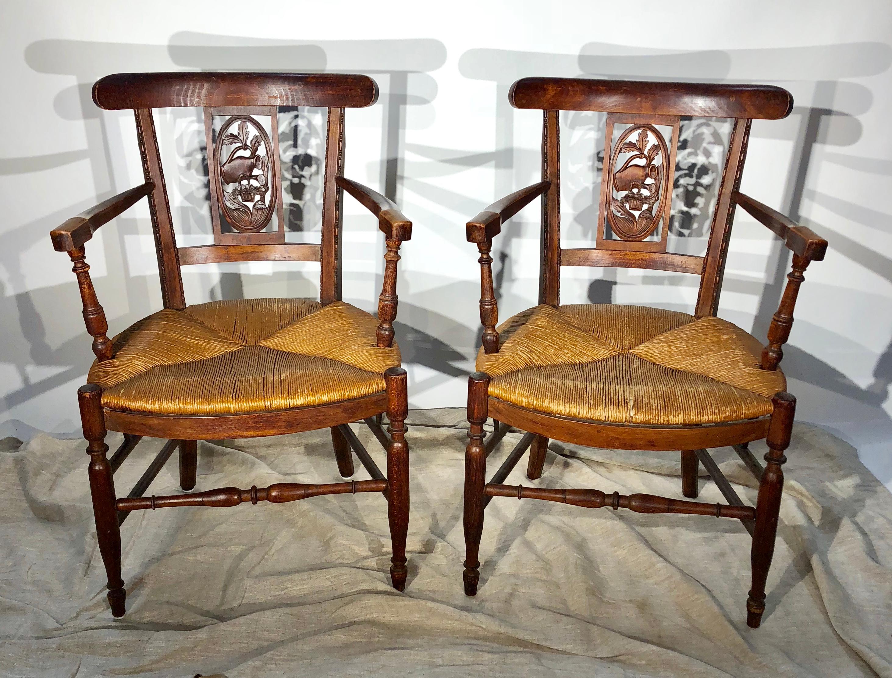 A pair of rush-seat armchairs, also called “bonne femme” chairs in beechwood, with yoke backs and carved panels with a gardening motif, circa 1870, French.