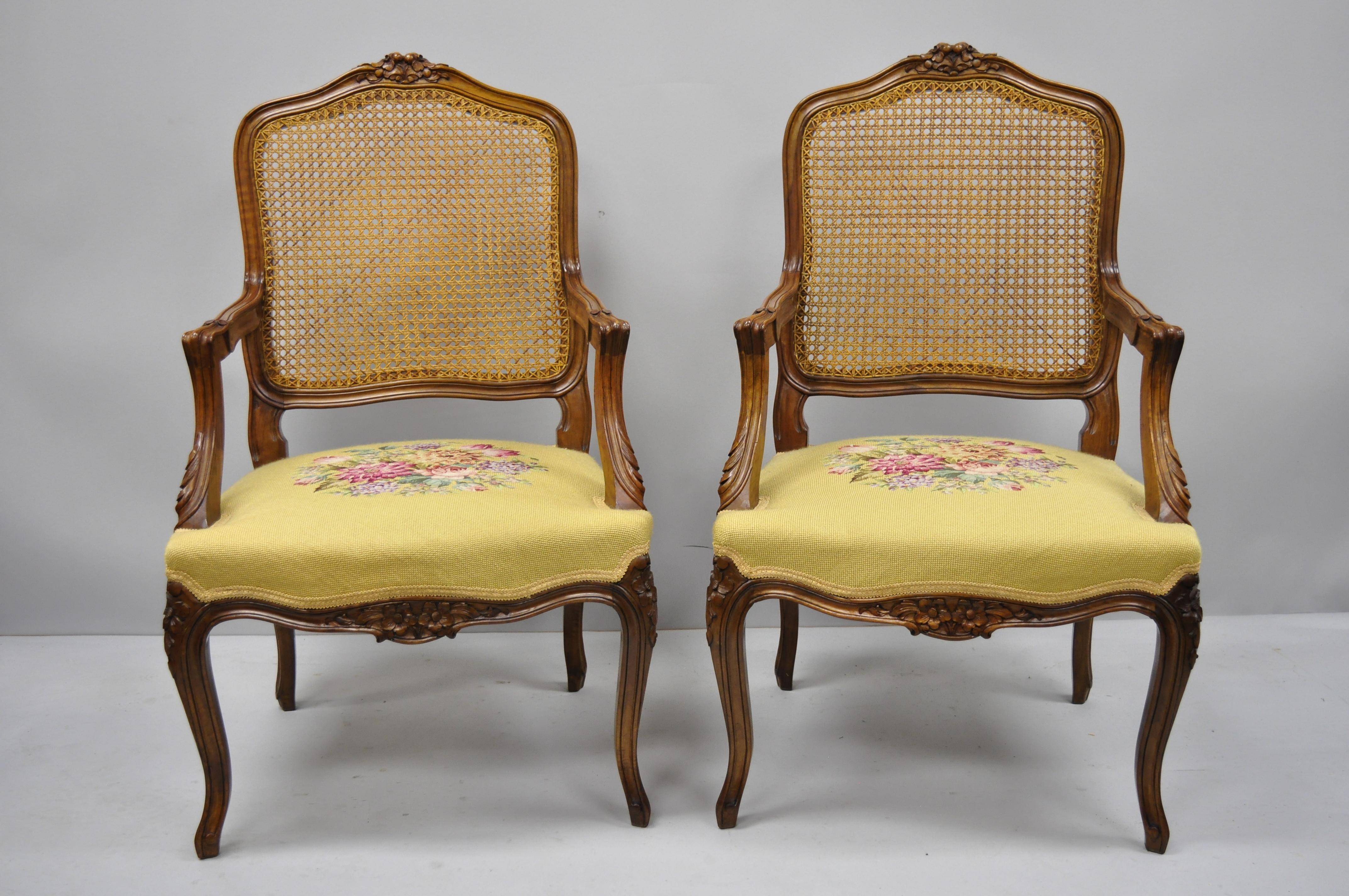 Pair of French Country Louis XV style cane back chair needlepoint armchairs. Items feature cane back, floral needlepoint upholstery, solid wood construction, nicely carved details, cabriole legs, great style and form, circa mid-20th century.