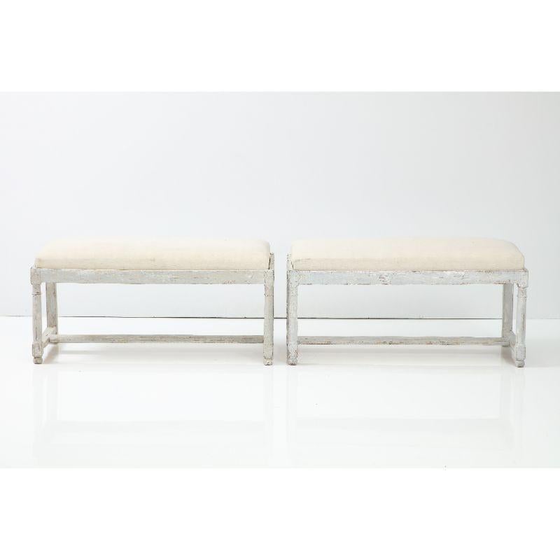 A pair of French Country benches painted in a pale blue-gray color. The front legs are turned with all legs having stretchers. The cushion is easily removed and is perfect for reupholstery.
