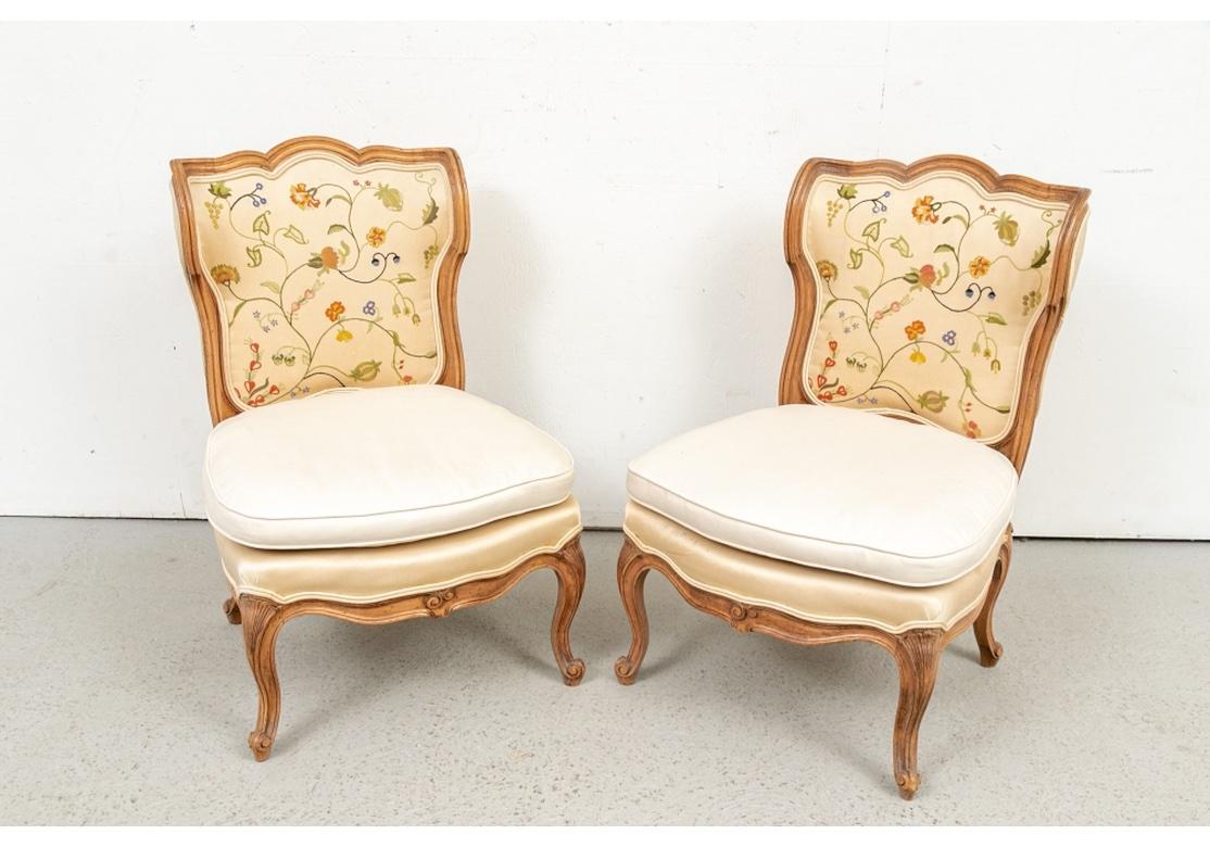 A pair of charming French country low slung slipper chairs. With elegant shaped crest rails and sides with slight wings on the ends. Wide comfortable seats, raised on cabriole legs with carved shell knees resting on Snail’s Head Foot and curved seat