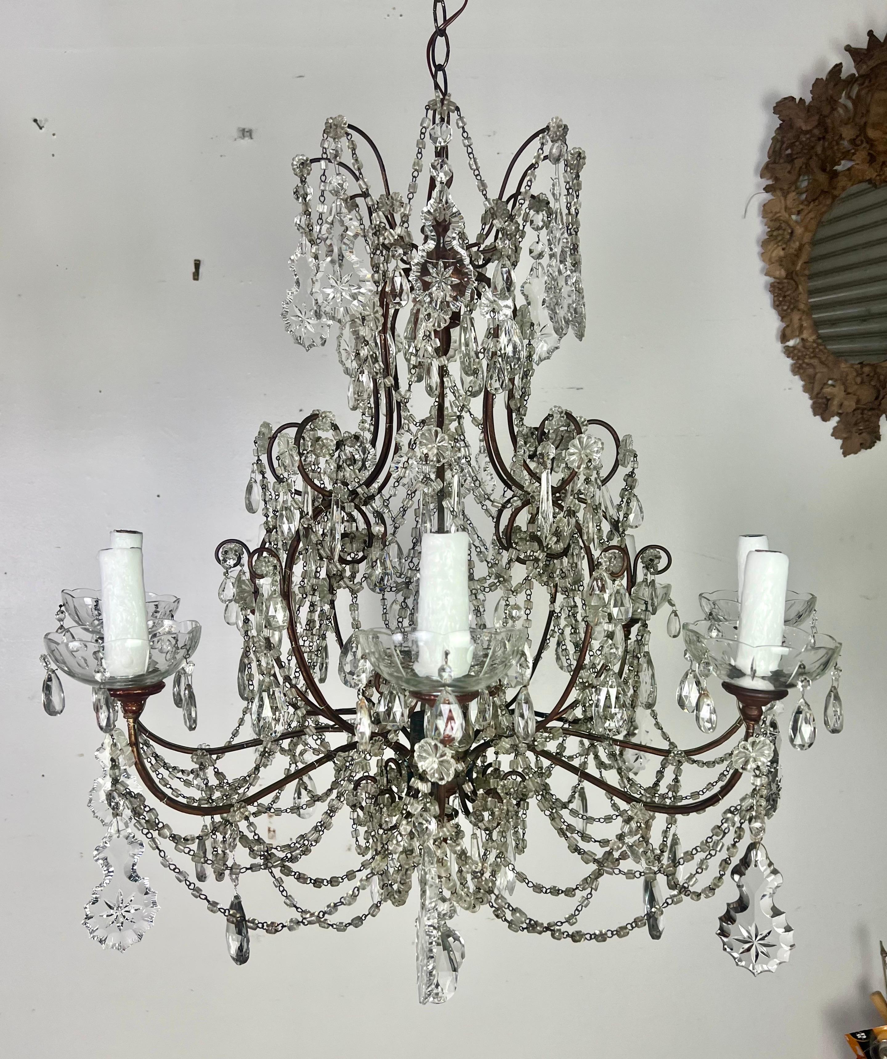 Pair of French 8-light crystal chandeliers featuring star-etched crystals and garlands of macaroni beads, giving them a unique and opulent look.  The use of a crystal finial in the center, along with gilt wood bobeches, adds to their elegant and