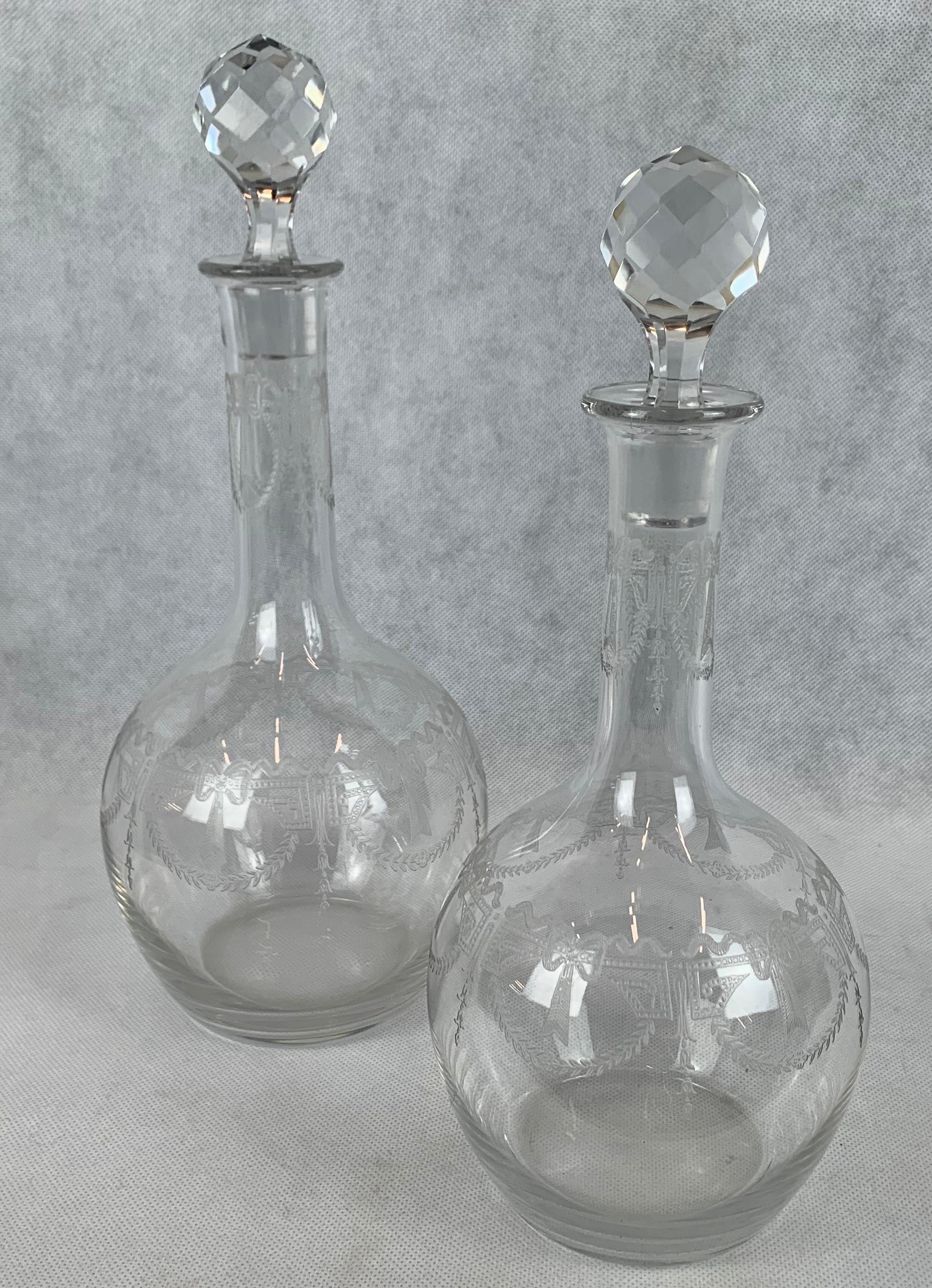Set of French crystal decanters each having engraved bodies and faceted stoppers. There is a polished pontil on the bottom of each decanter. The design is swags of laurel leaves and curling ribbons and bows. The pair were probably part of a larger