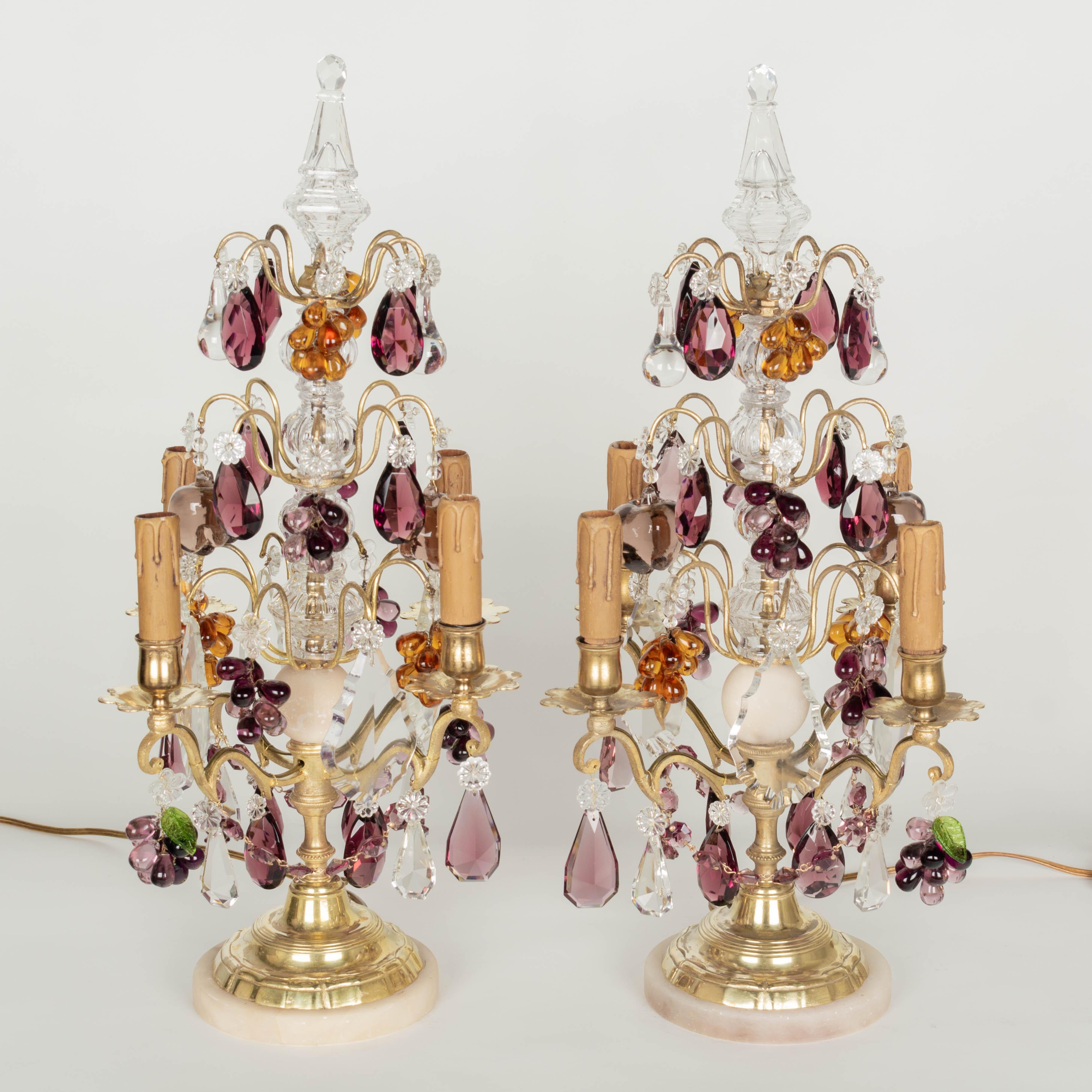 A pair of Louis XV style four-light French girandoles, or chandelier table lamps. Made of cast polished brass with three tiers of clear and amethyst cut crystal prisms, amber and amethyst grape clusters, and large glass apples. Center post with