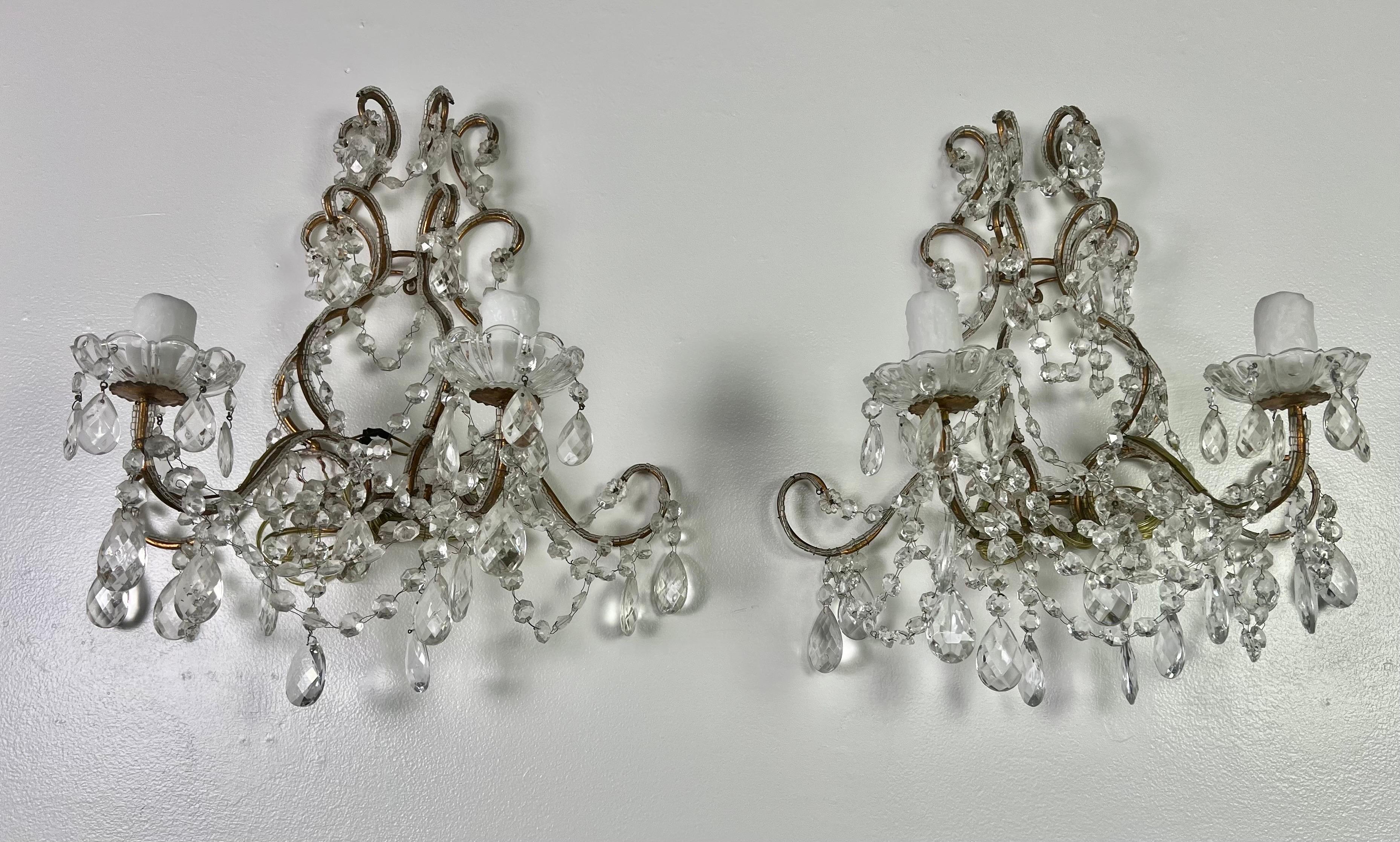 Pair of French crystal gilt metal 2-light sconces. The sconces are adorned with faceted almond shaped crystals and garlands of English cut beads. The sconces are newly rewired with drip wax candle covers.
