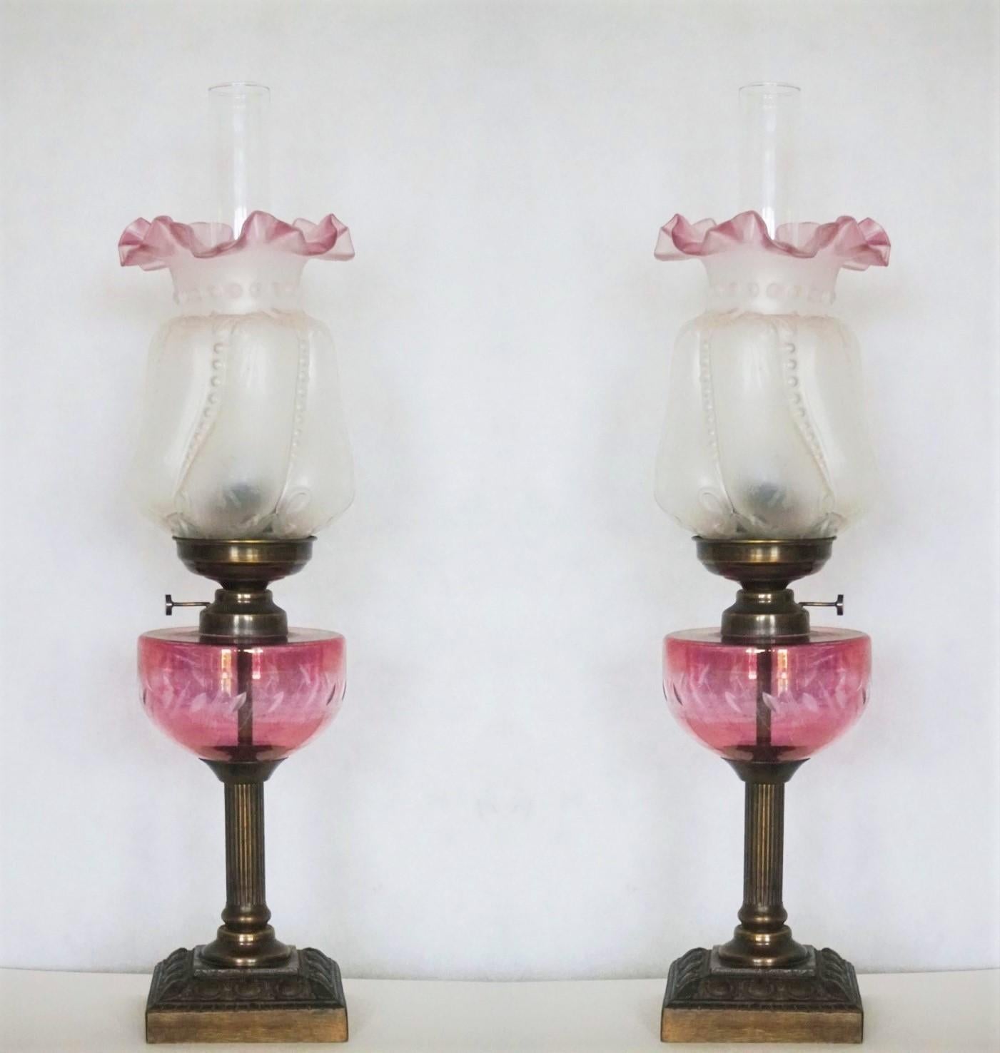 A lovely pair of electrified cranberry colored cut-glass font oil lamps raised on a patinated bronze fluted column, all on a solid bronze square base, France, circa 1910-1920. With beautiful etched art glass shades and clear glass hurricane