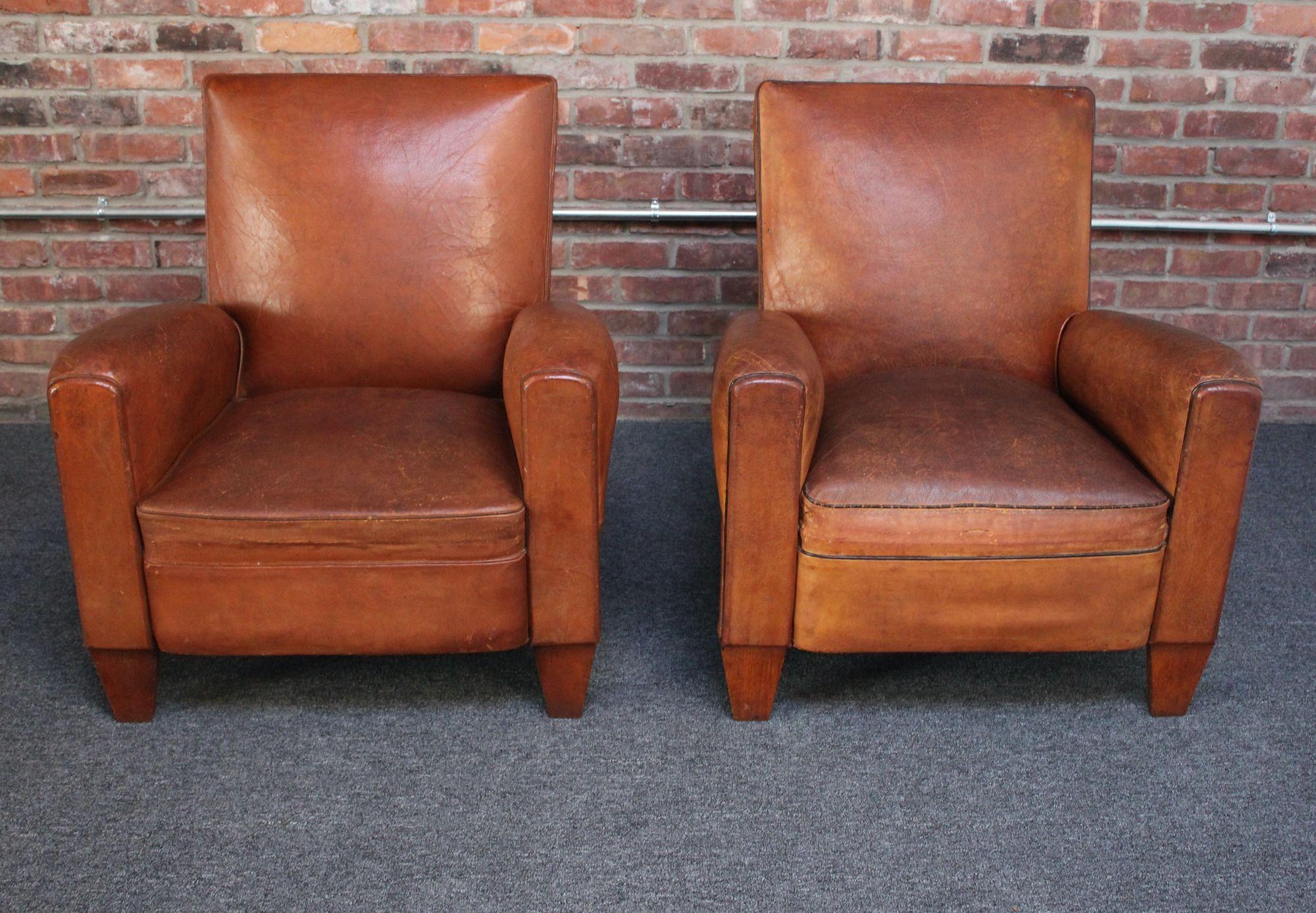 Handsome pair of 1940s French club chairs sourced in the south of France in supple sheep hide leather with squared-back forms and nailhead decoration to the back border, all supported by triangular wedge-feet in the front and carved, slightly angled