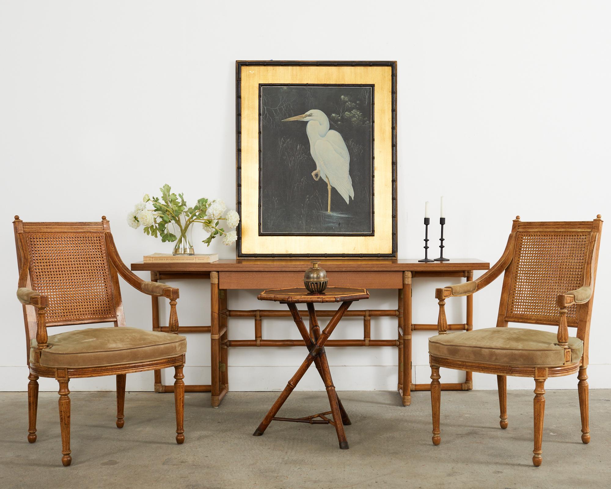 Distinctive pair of late 20th century caned armchairs or fauteuils made in the French directoire taste. The chairs feature a square back with a double-caned seat back. The arms gracefully curve down to a generous round seat with a suede leather