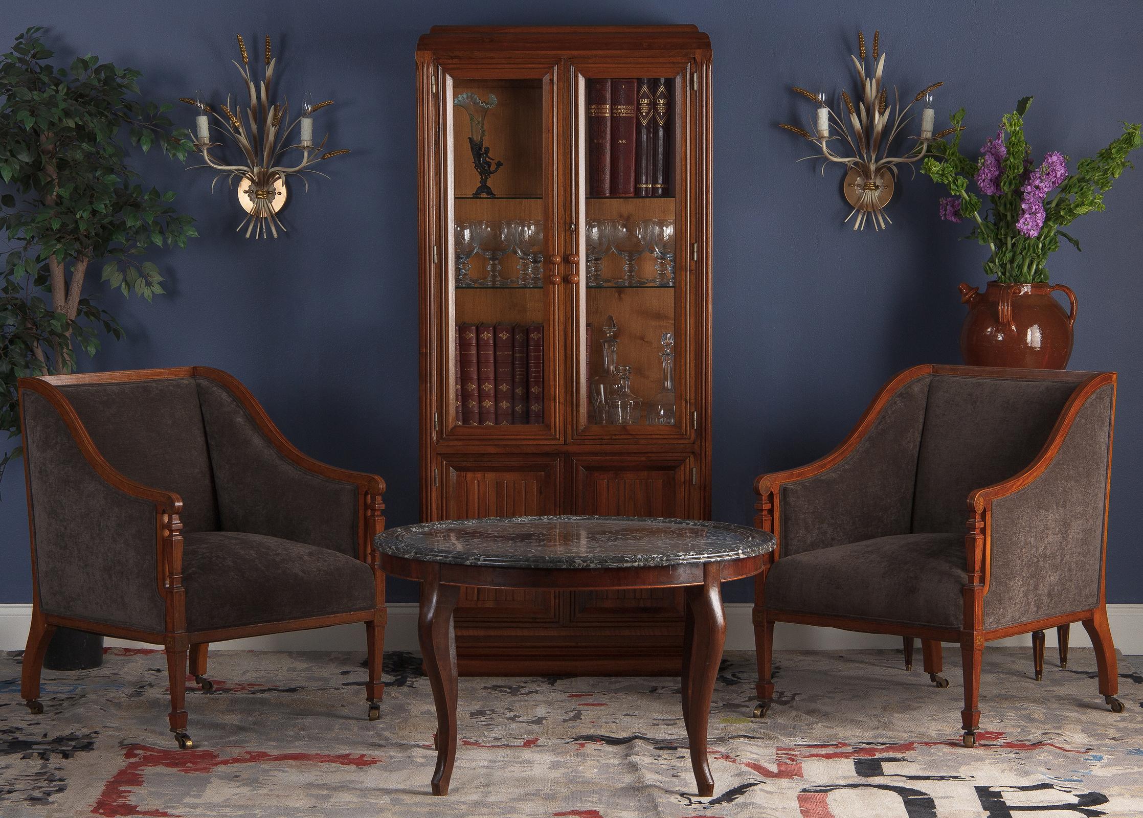 A phenomenal pair of French upholstered mahogany armchairs in the Directoire style, circa 1890. The bergère have a square form with elegant, sloping arms that end in scrolled hand rests. Exquisitely carved square balusters form the front legs, with