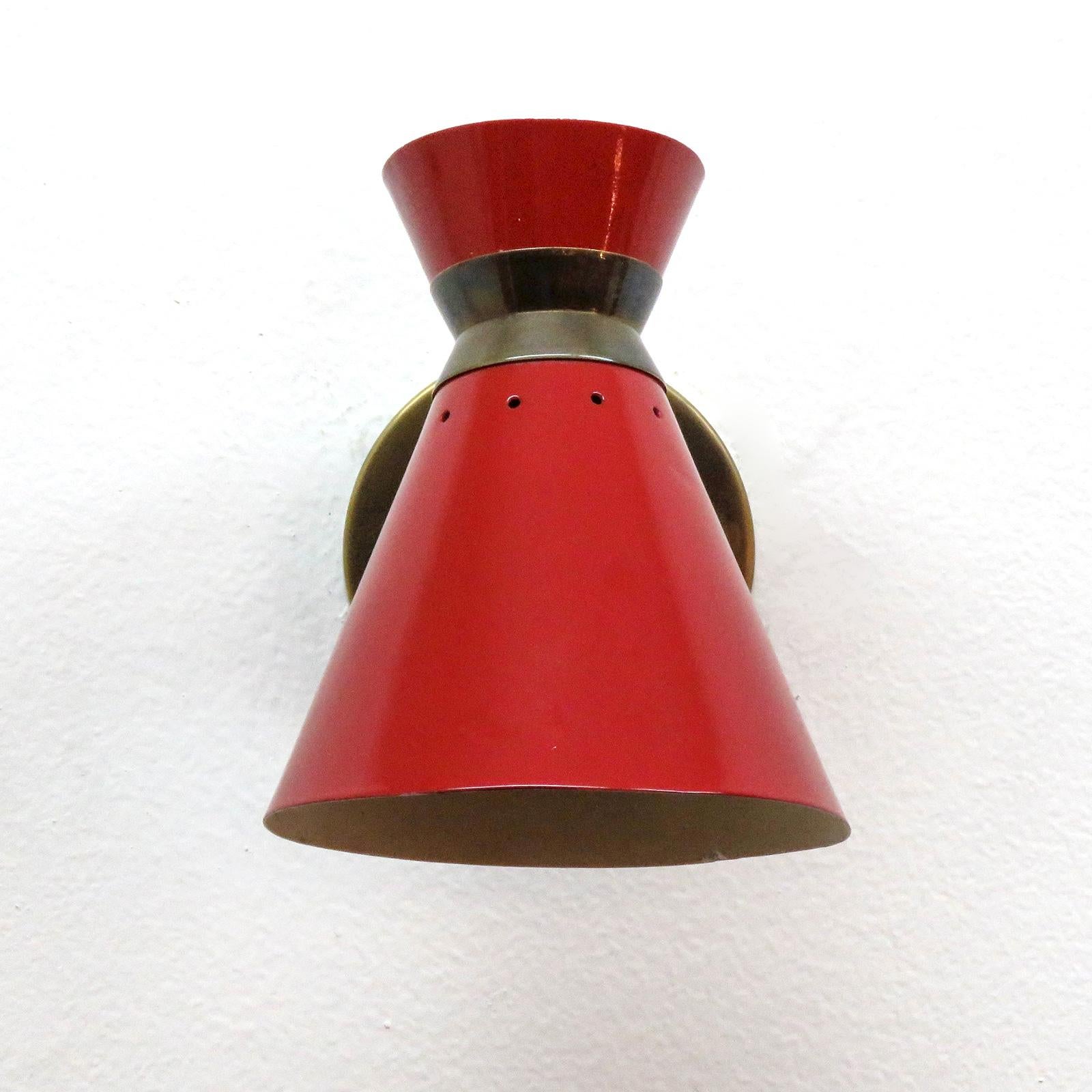Elegant pair of French short stem double cone wall lights by Rene Mathieu in red enamel and brass, individual on and off switch, some wear to the interior enamel, wired for US standards, one E12 socket per fixture, max. wattage 60w each, bulbs