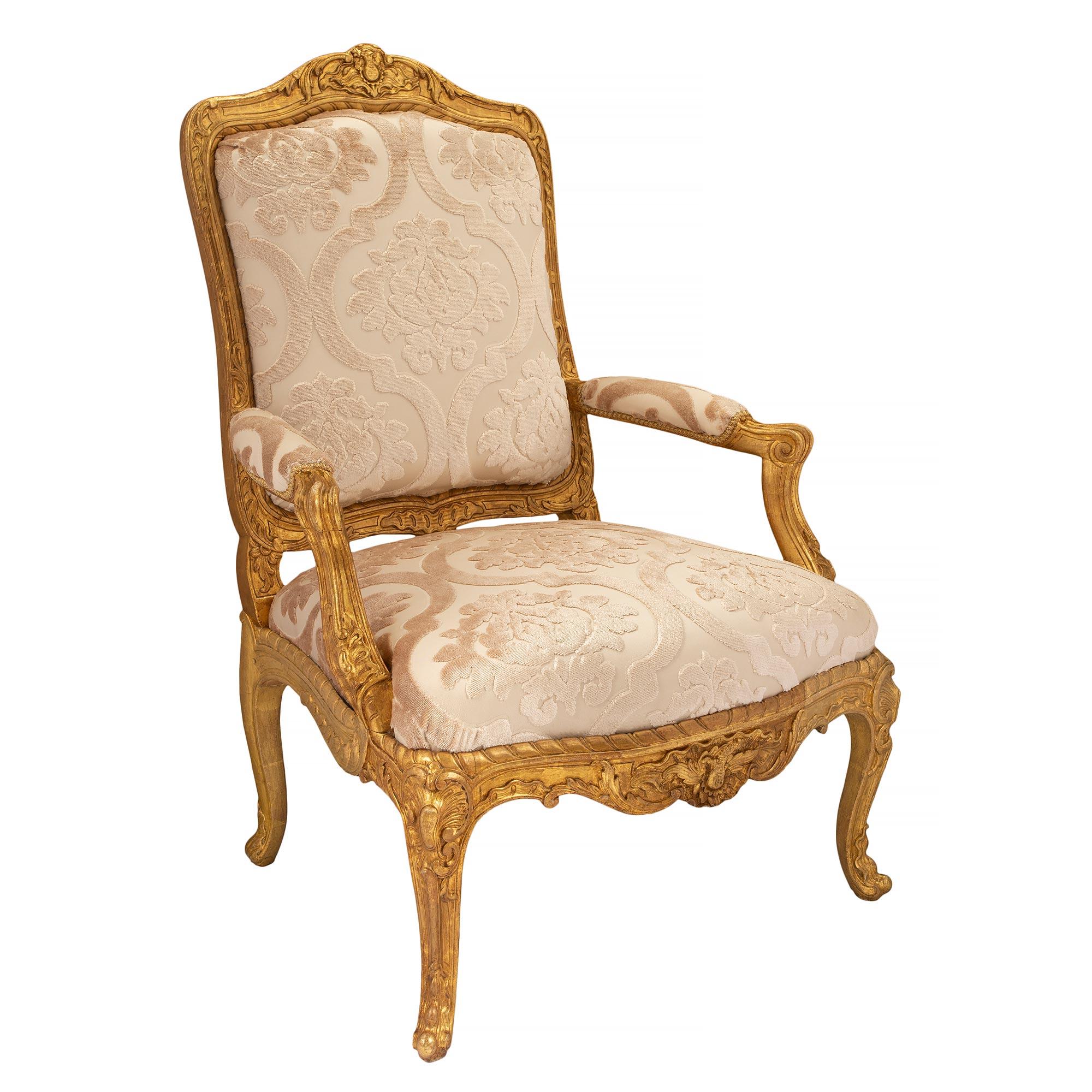 A beautiful and high quality pair of French early 19th century Louis XV st. giltwood armchairs. Each armchair is raised by elegant cabriole legs with lovely carved foliate designs and finely carved cabochons at each corner. The decorative arbalest