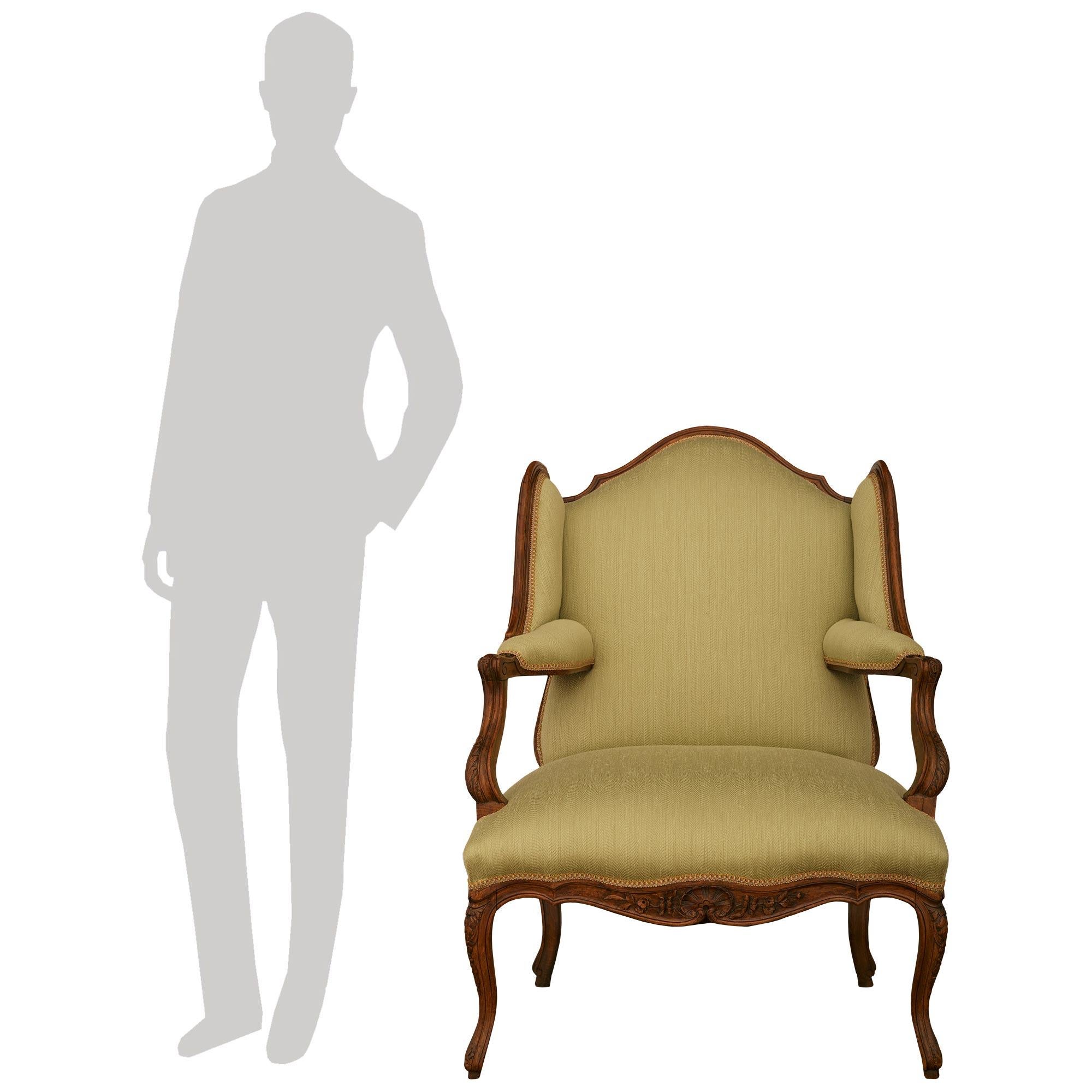 Paire de fauteuils en noyer de style Louis XV du début du XIXe siècle. Cette magnifique paire de Bergères À Oreilles repose sur quatre pieds cabriole avec des décors feuillagés sculptés en bas et en haut. Le tablier avant chiné et festonné présente