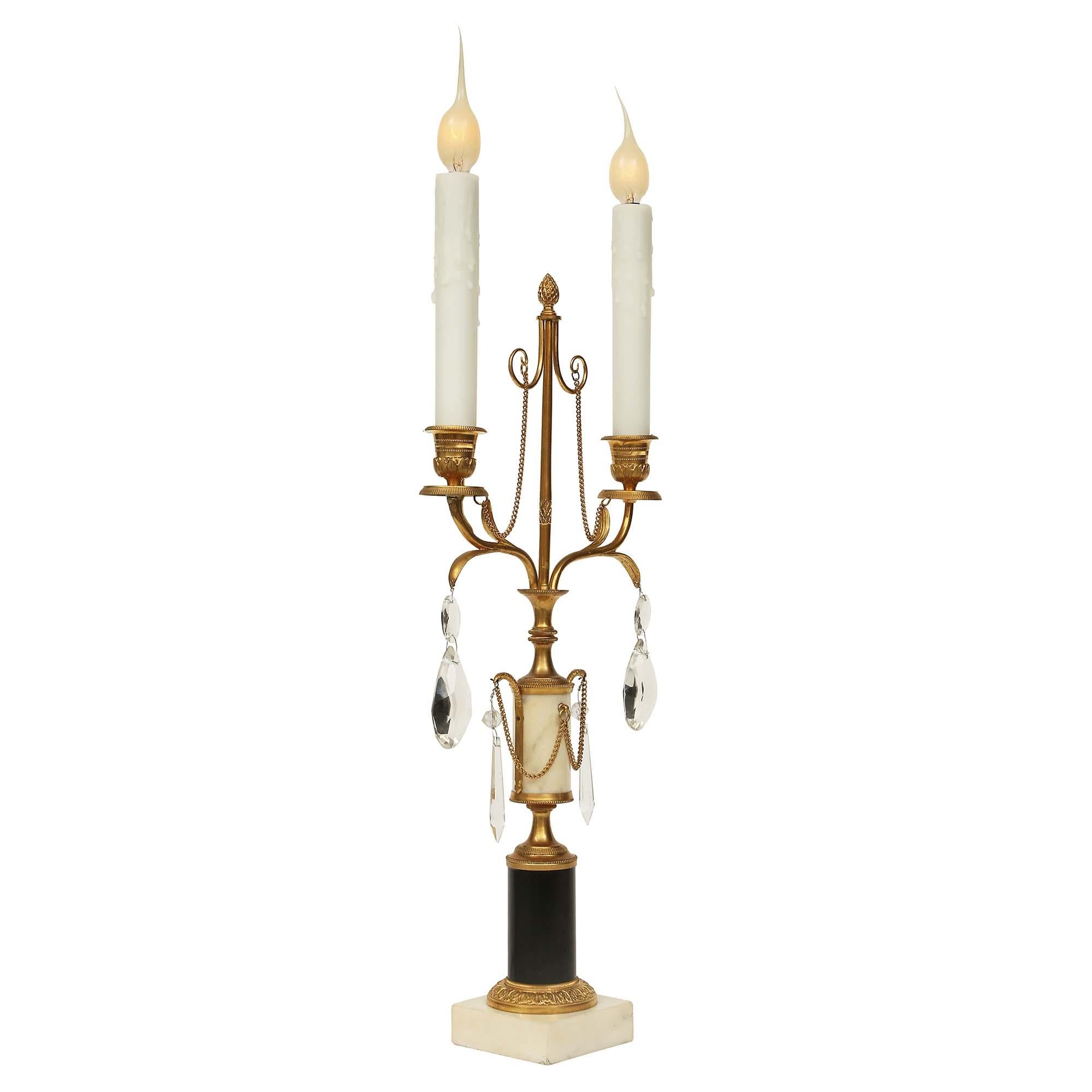 An elegant pair of French early 19th century Louis XVI style with white carrara and black Belgian marble and ormolu two light candelabras. The pair are raised by a square white Carrera marble base below a black Belgian marble plinth, decorated with