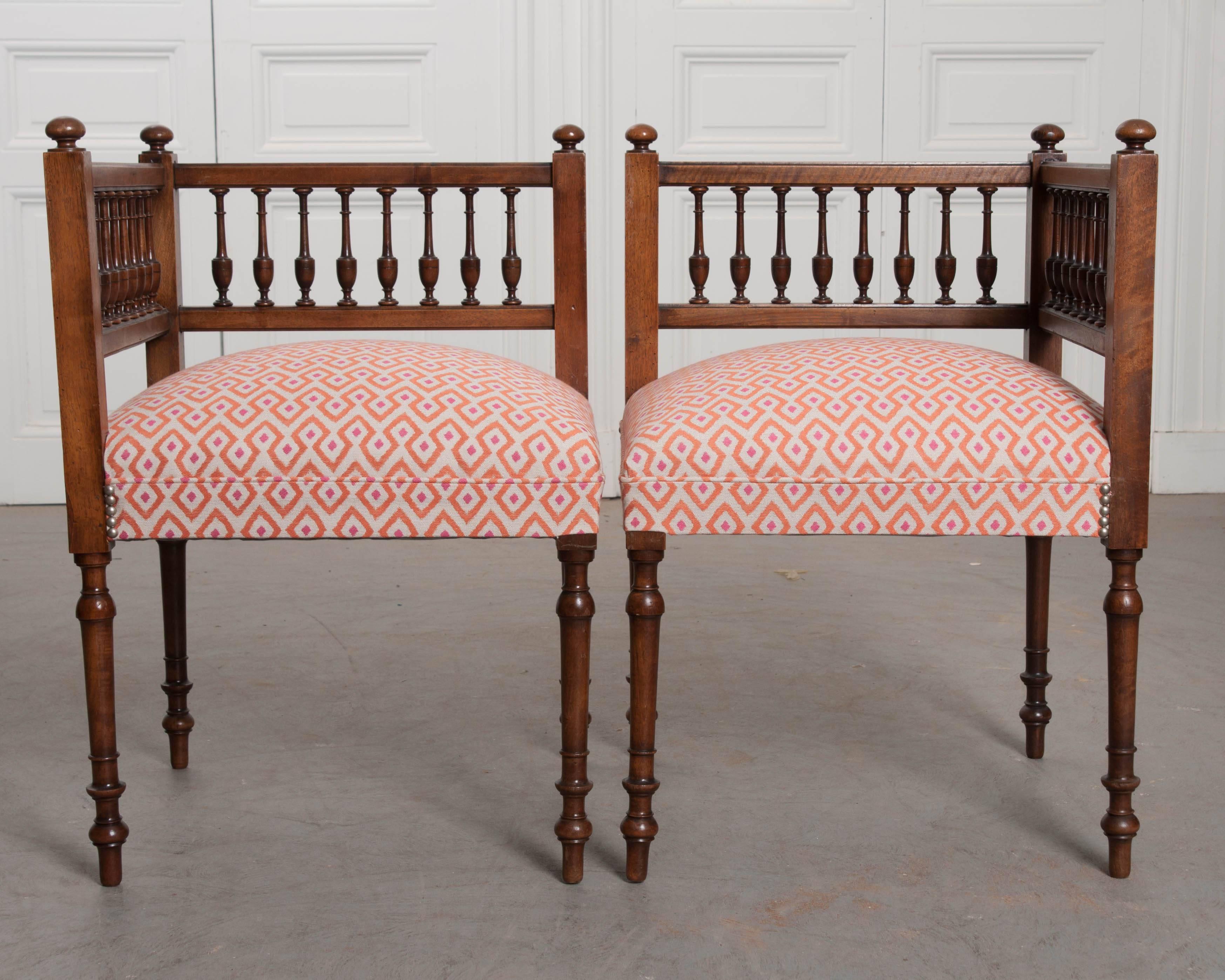 A darling pair of mahogany corner stools, made in early 20th century, France. The set has been recently upholstered in a geometric patterned fabric in a pink and orange colorway. The chairs have low, turned balustrade backs that have joinery topped