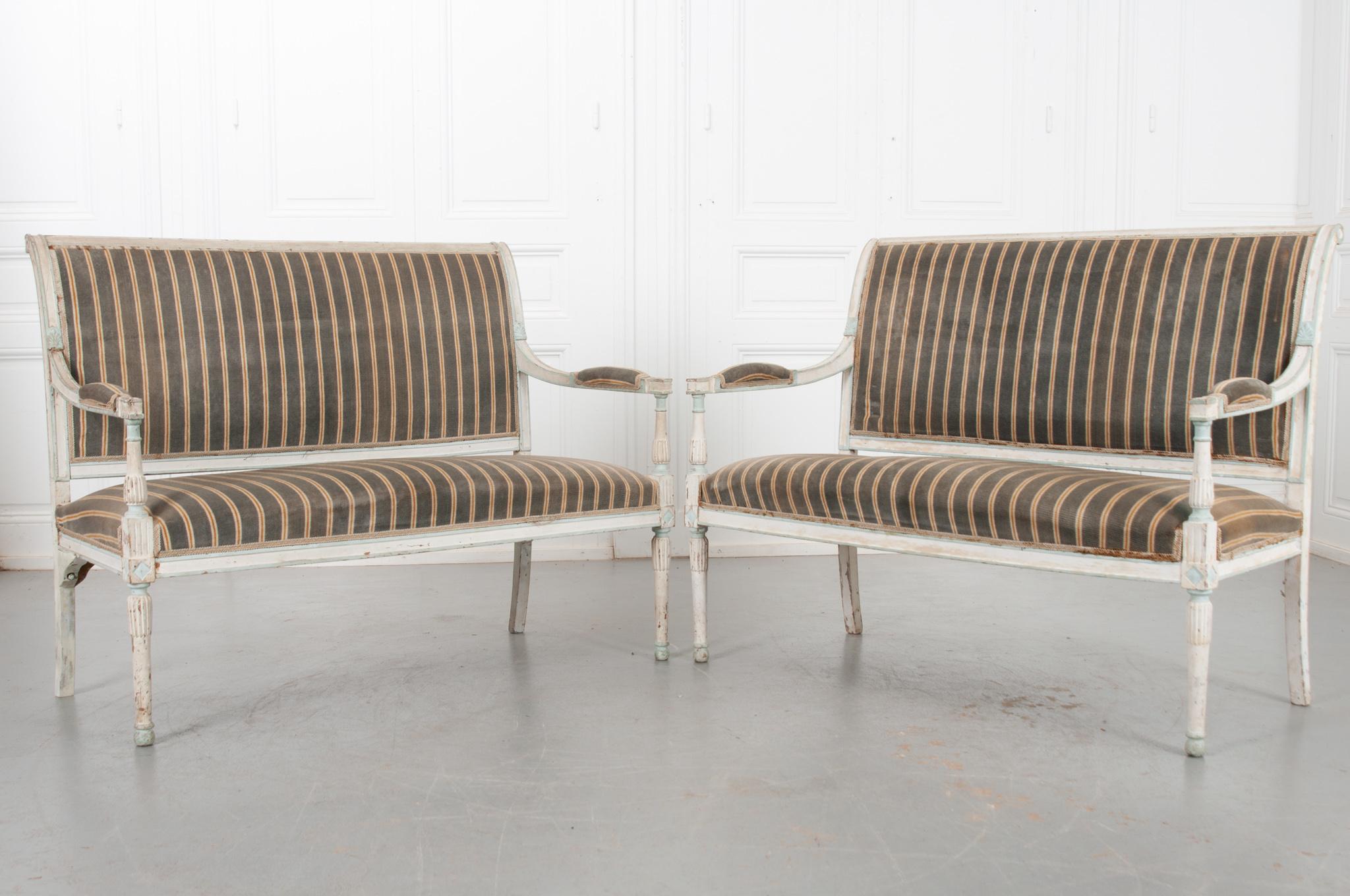 A stunning pair of painted and upholstered banquettes from early 20th century France. The pair have beautifully carved details covering their cream-painted frames which have been accented where light-blue paint has been applied. The finish has