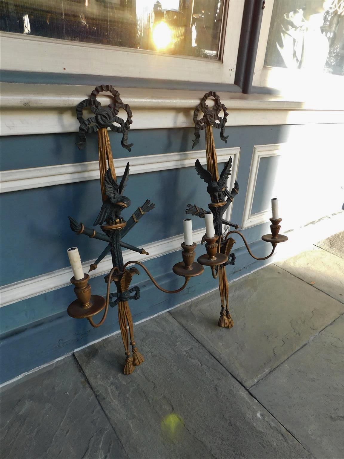 Pair of French flanking ebonized eagle and ribbon gilt carved wood and gesso two arm torchere, quiver, and tassel wall sconces, Mid-19th Century. Pair were originally candle powered and have been electrified.